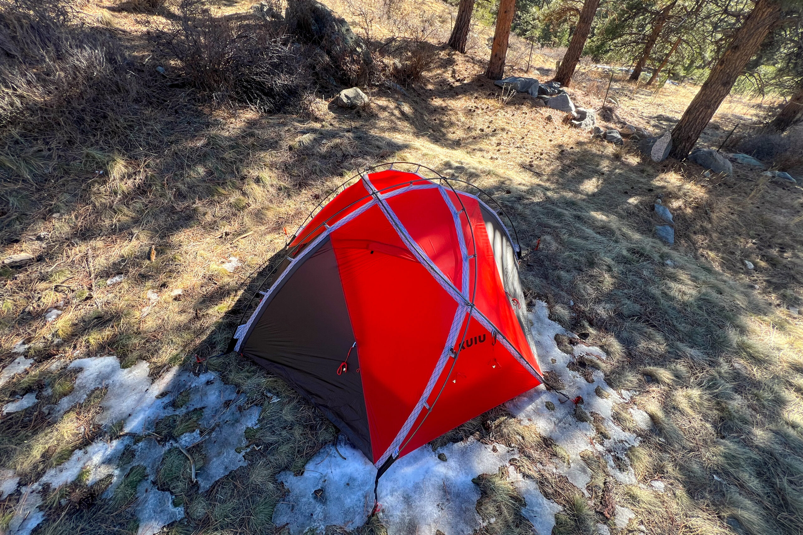 Aerial view of the KUIU Storm Star 2 tent pitched on a forest floor with patches of ice and grass.