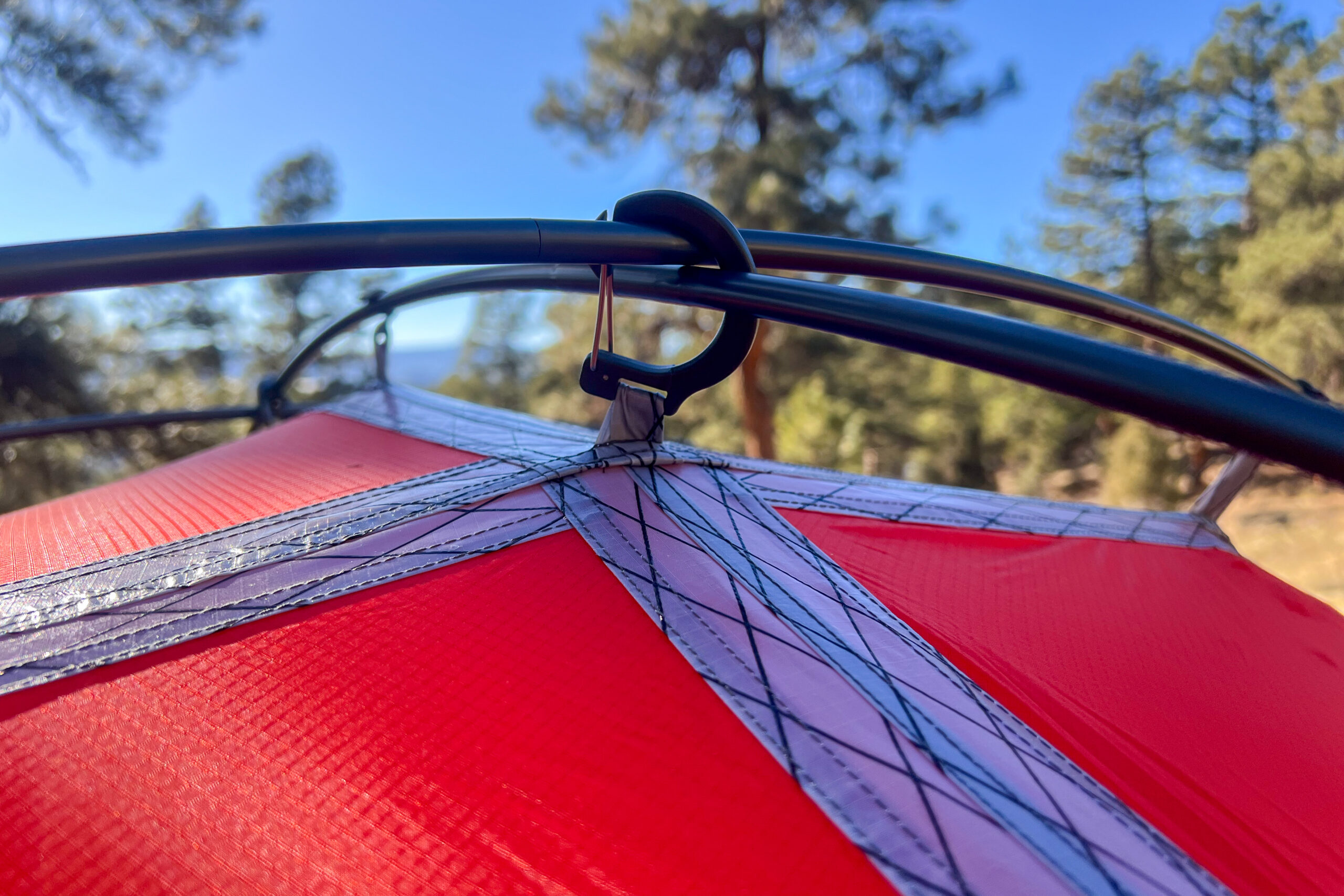 Close-up of the tent’s pole intersection with black and silver reinforcements, set against a sunny forest backdrop.