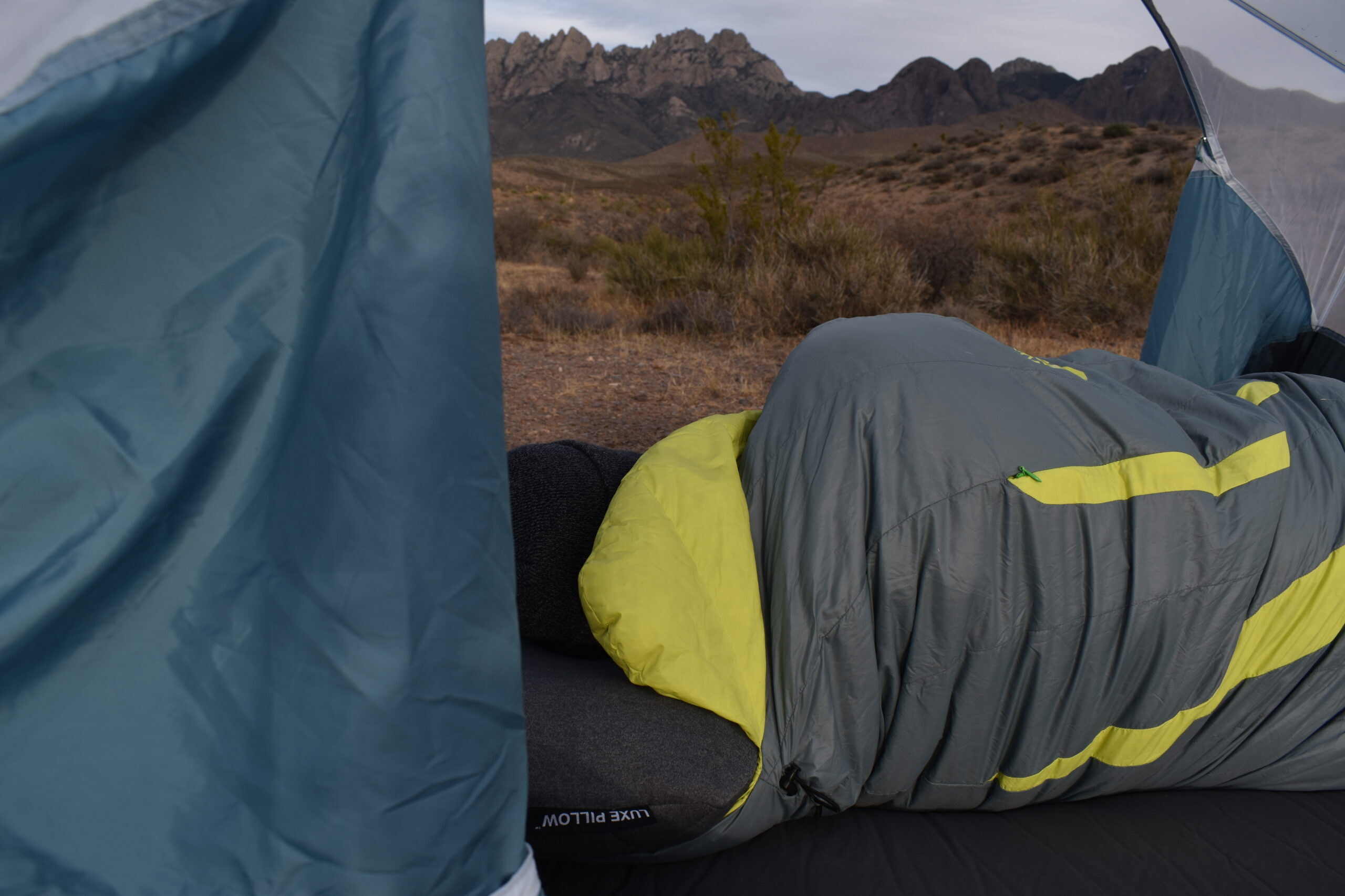 The author sleeping on the Klymit LUXE Camp Pillow while laying in a sleeping bag with mountains visible through the tent's mesh walls.