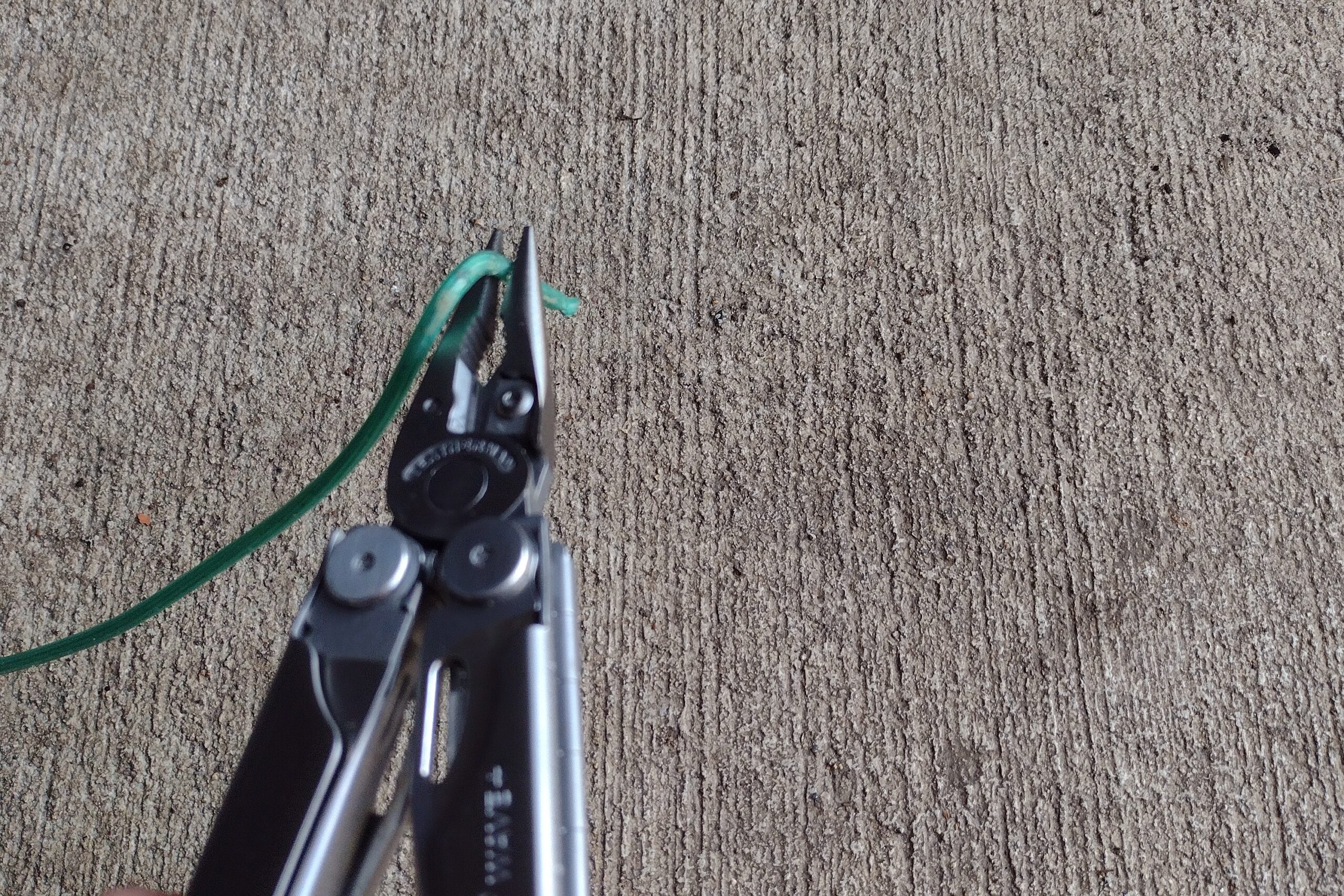 The Leatherman Wave+ with its pliers bending a green electrical wire.