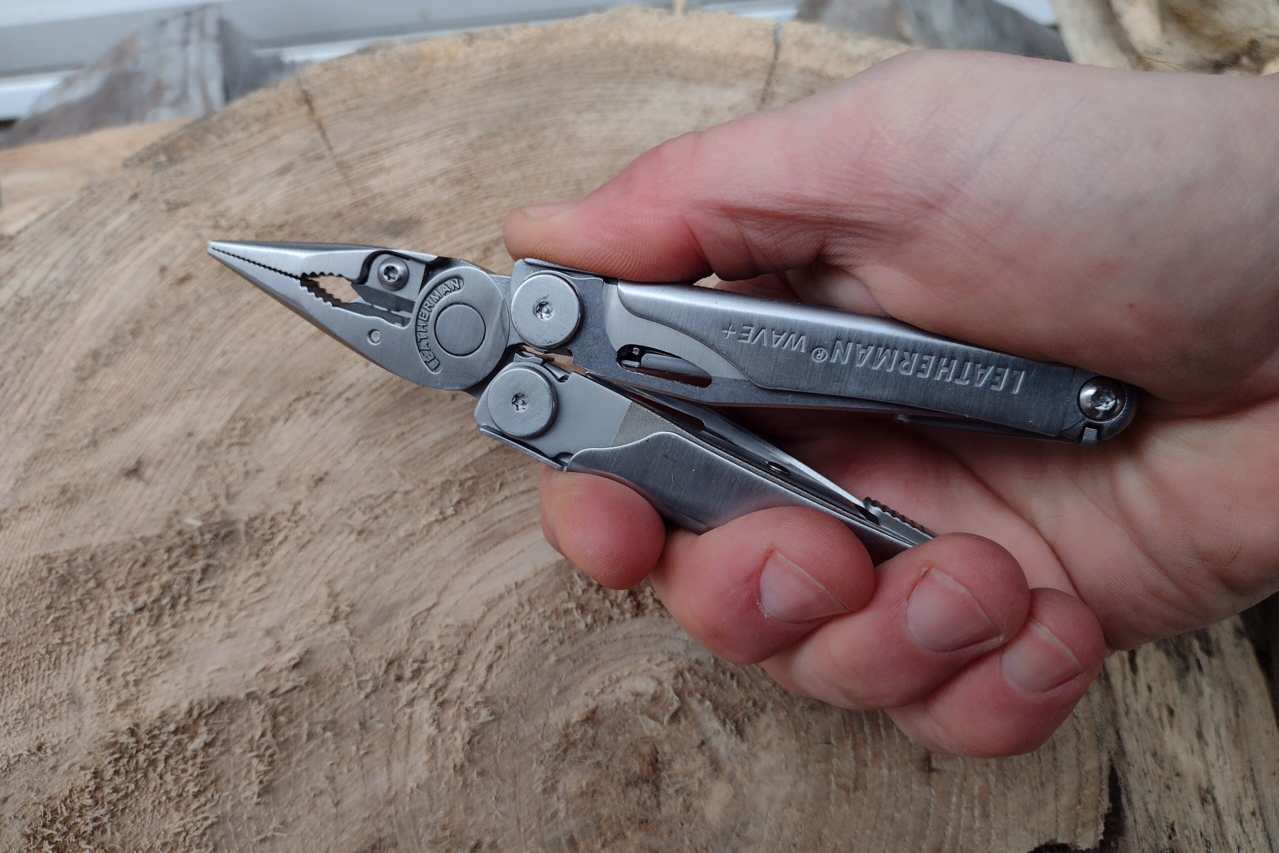 The Leatherman Wave+ held in hand above a log.