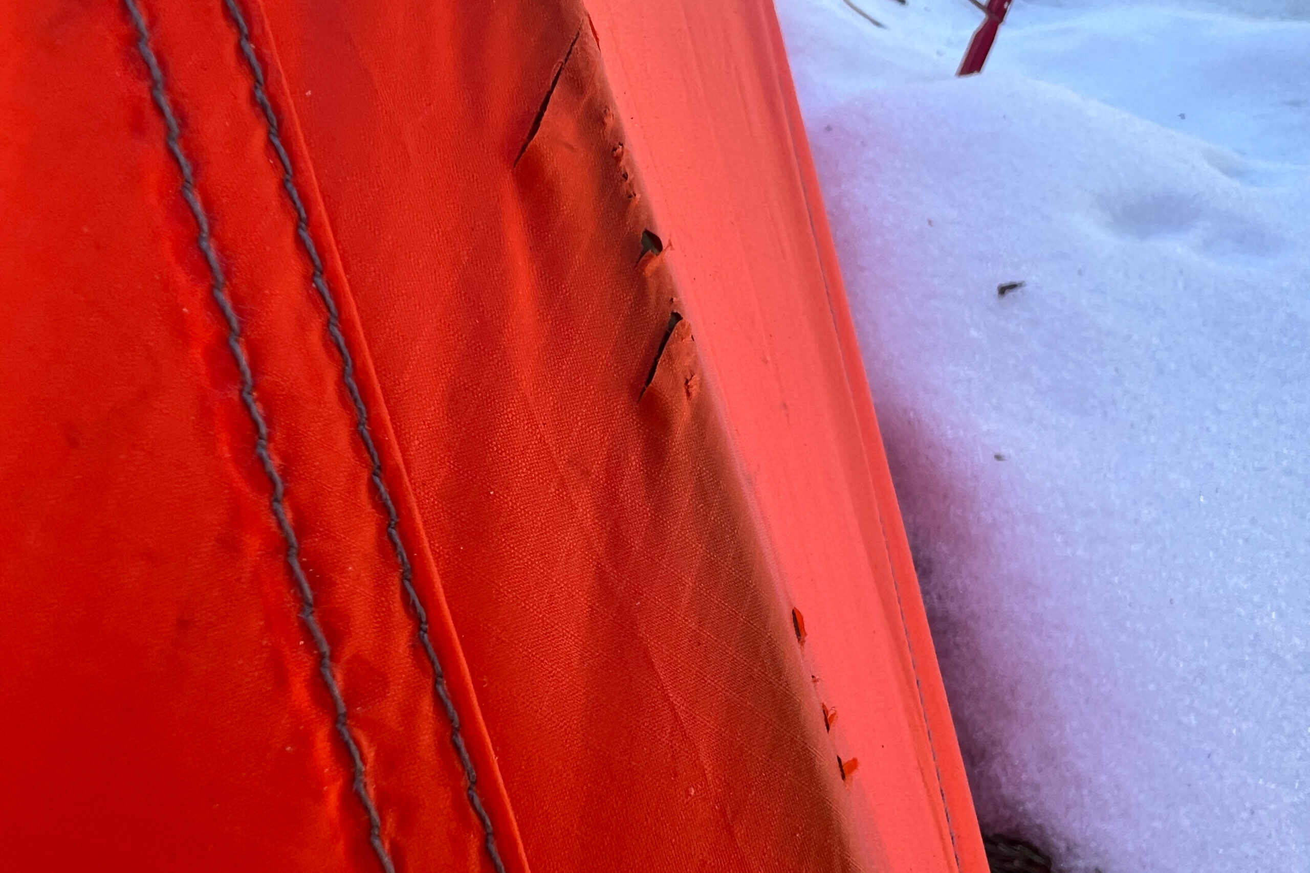 Close-up of a small tear in the rainfly of the MSR Access 2 tent, with snow visible in the background.