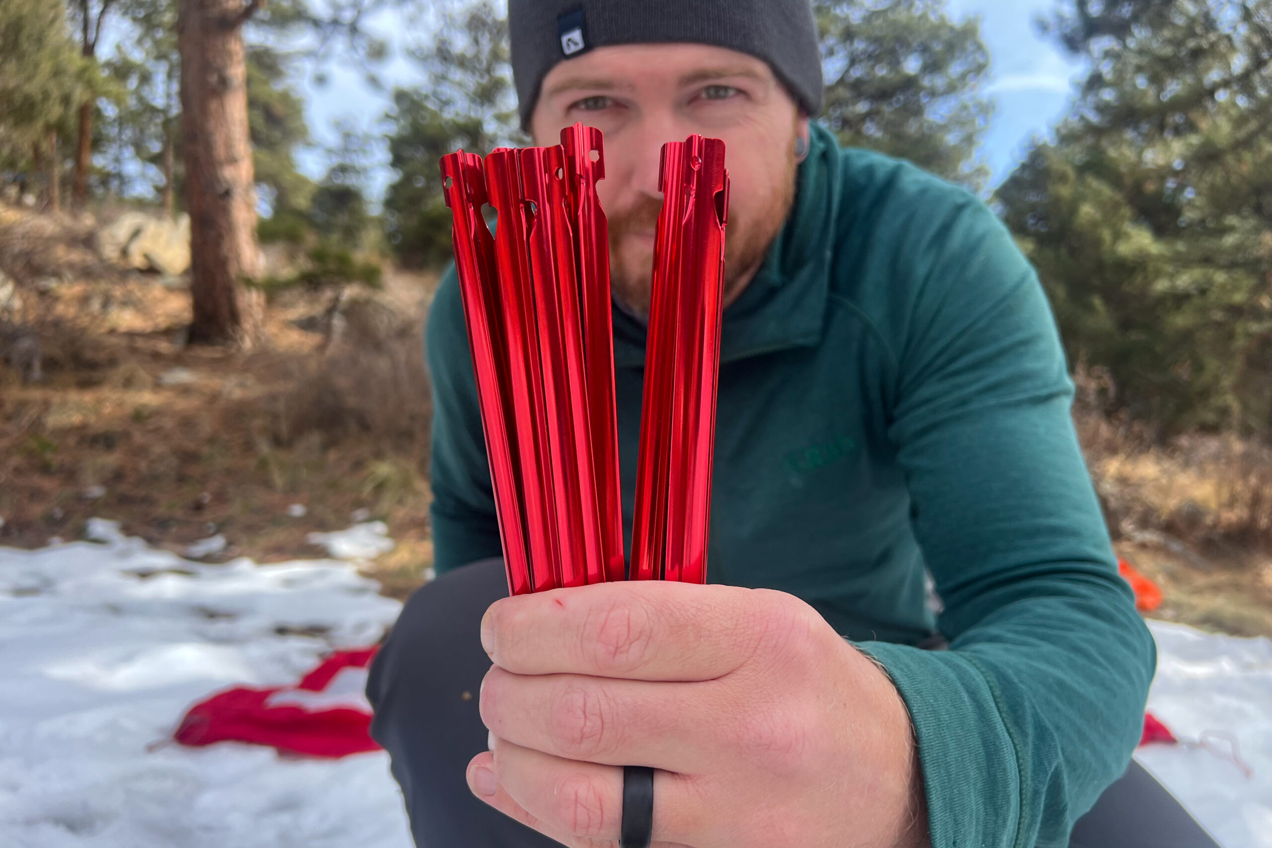 A close-up shot of MSR tent stakes being held in hand with snowy trees in the background.