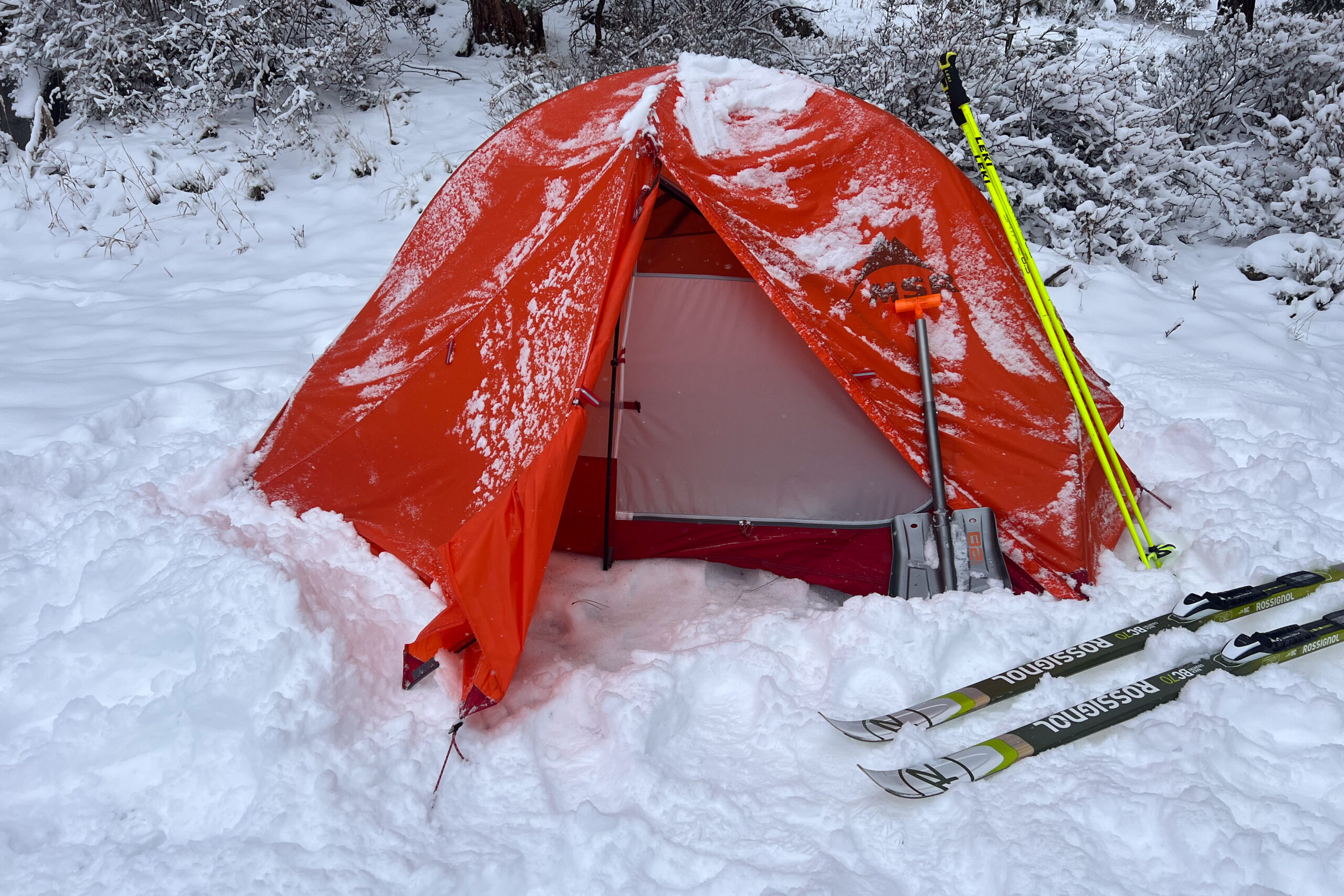 The MSR Access 2 tent pitched in snow, with skis and a snow shovel propped against the tent.