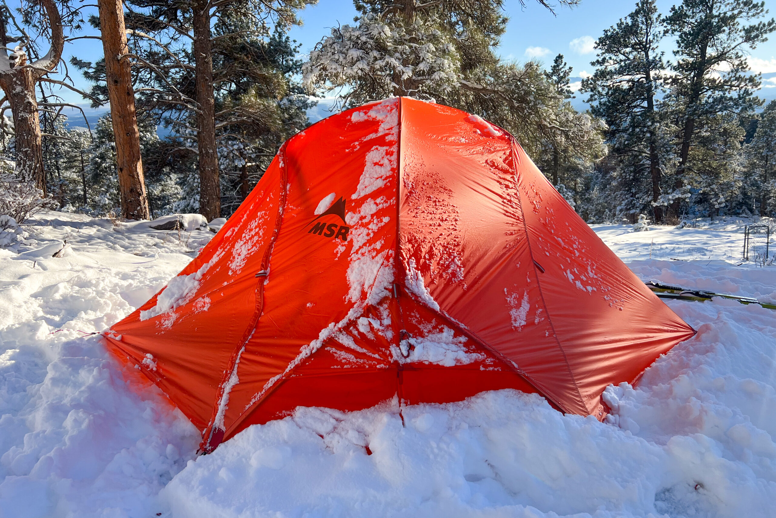 Side profile of the MSR Access 2 tent in the snow with trees and mountains in the background.