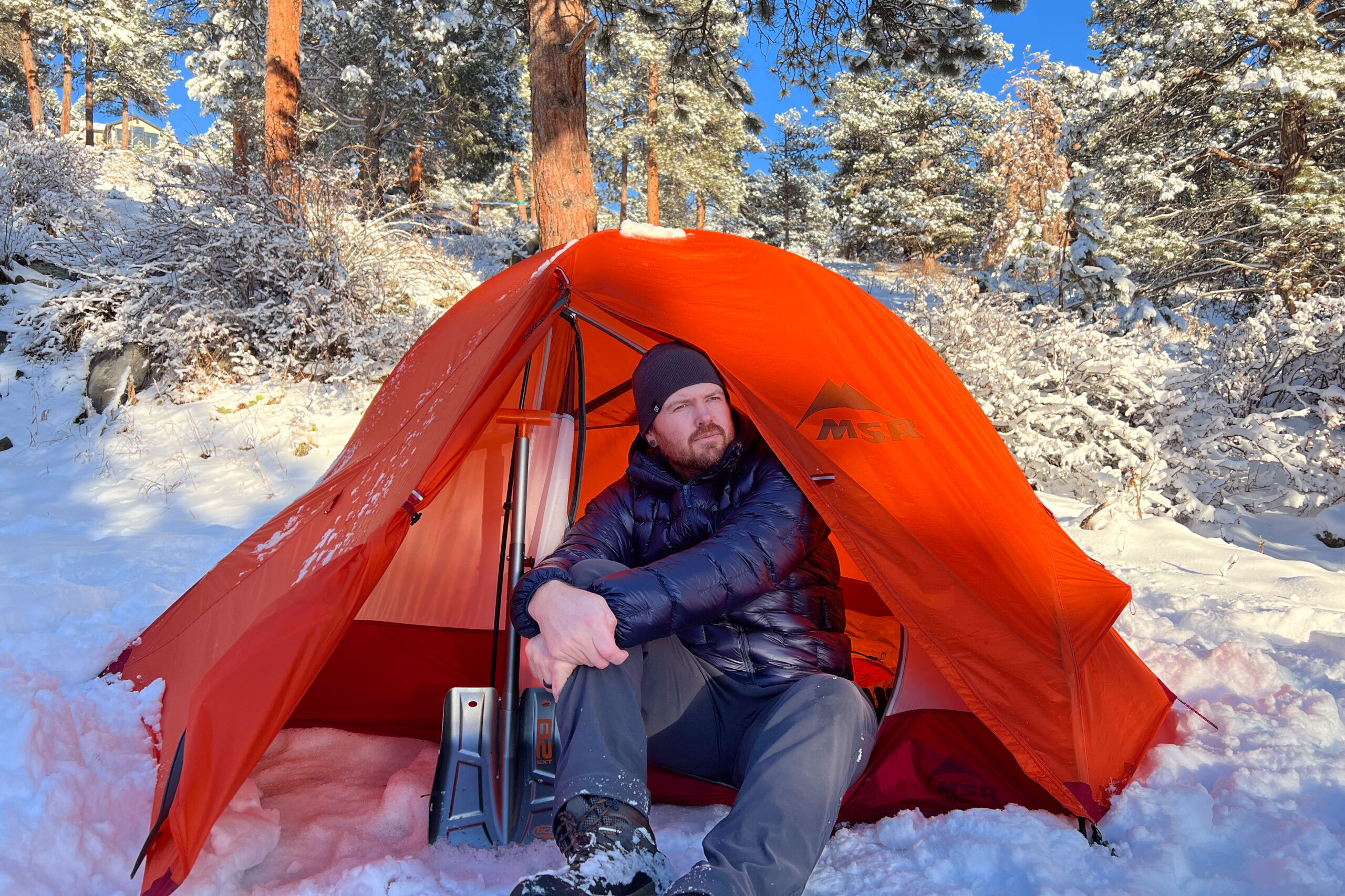 A person sitting in the doorway of the MSR Access 2 tent surrounded by fresh snow.