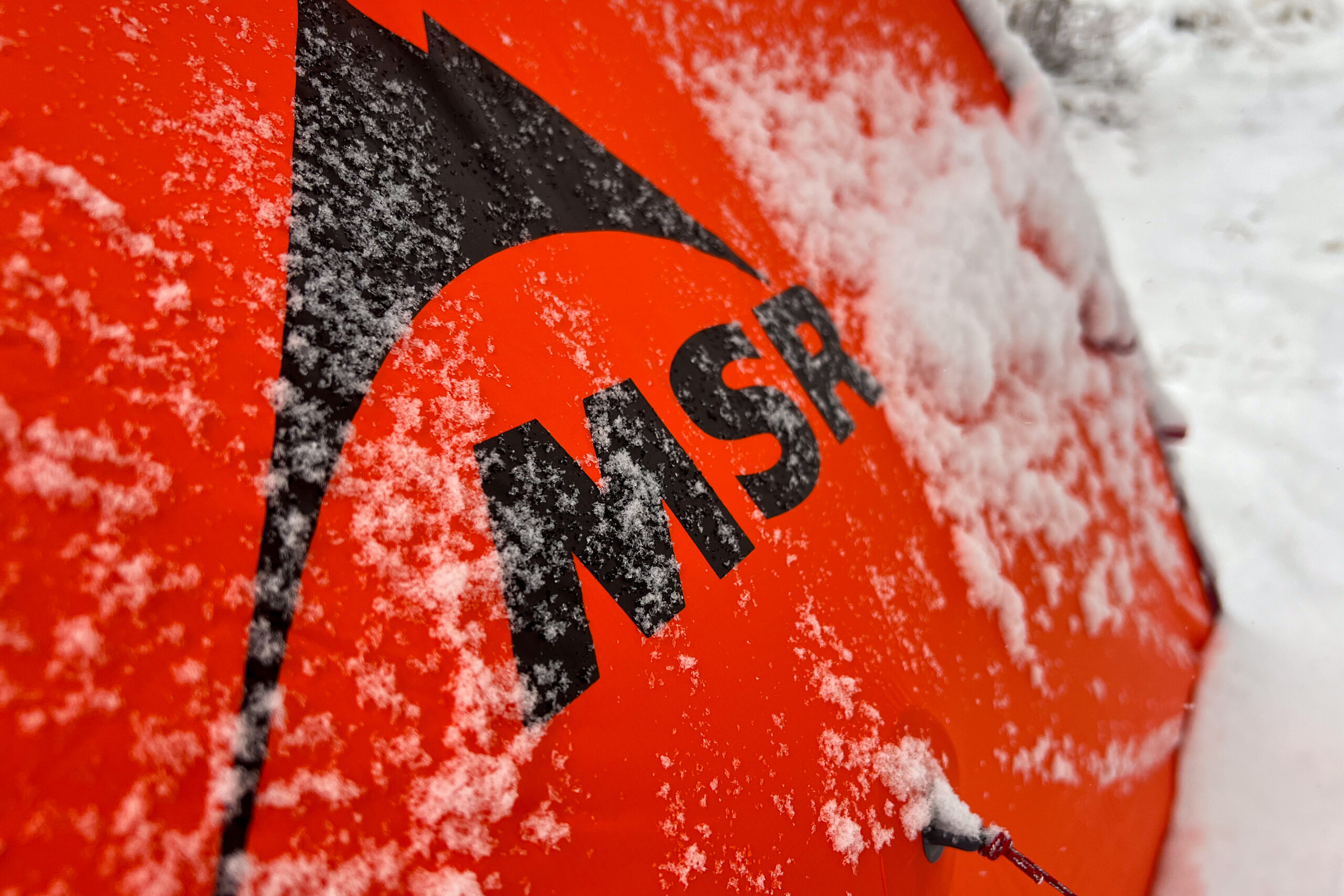 The MSR logo printed on the orange fabric of the Advance Pro 2 tent, partially covered with snow.