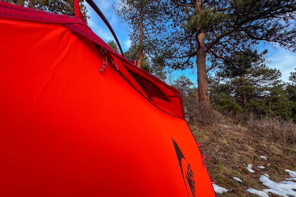 A side view of the vent flap on the MSR Advance Pro 2 tent, showing its durable construction against a backdrop of blue sky and pine trees.