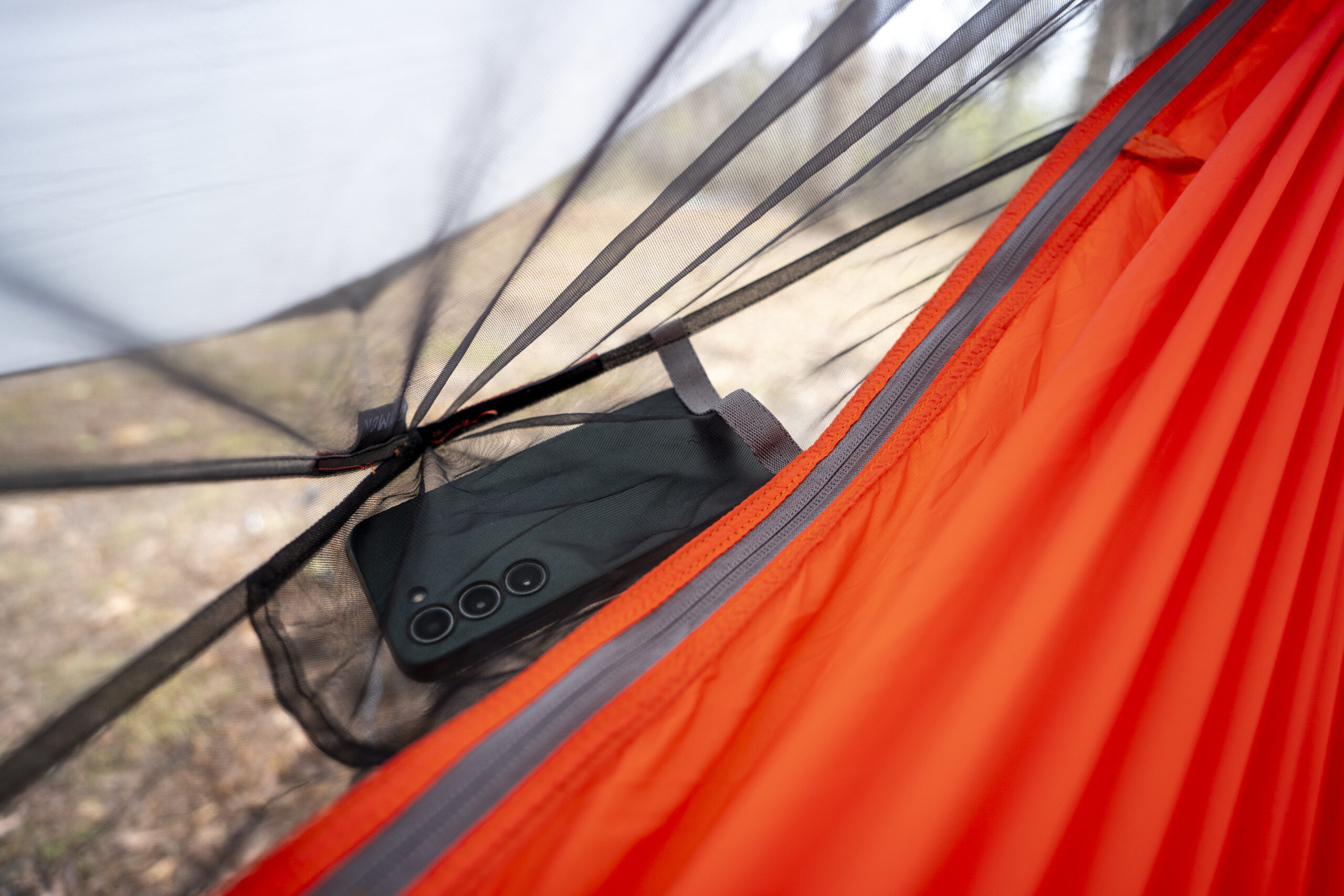 A phone rests in a mesh pocket on the interior of a hammock