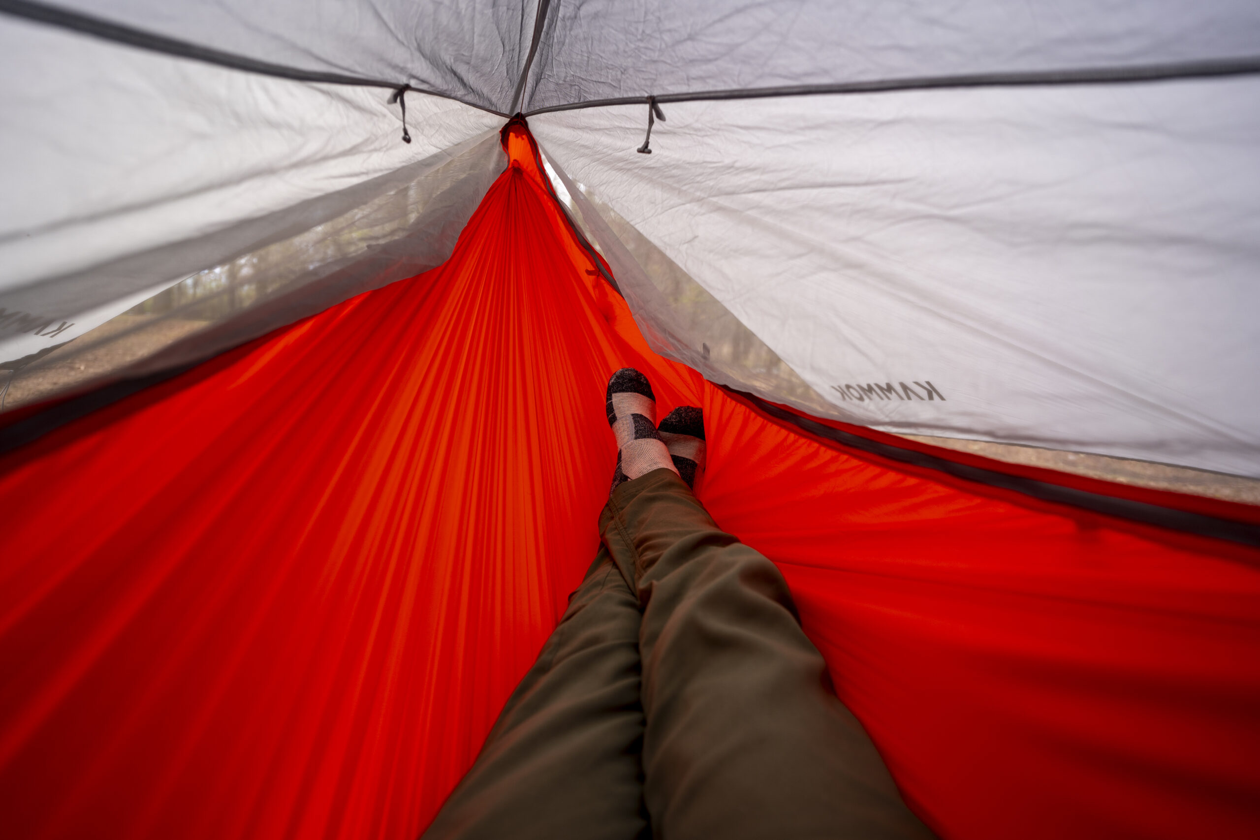 A pair of legs stretch out into an orange hammock from a point of view perspective