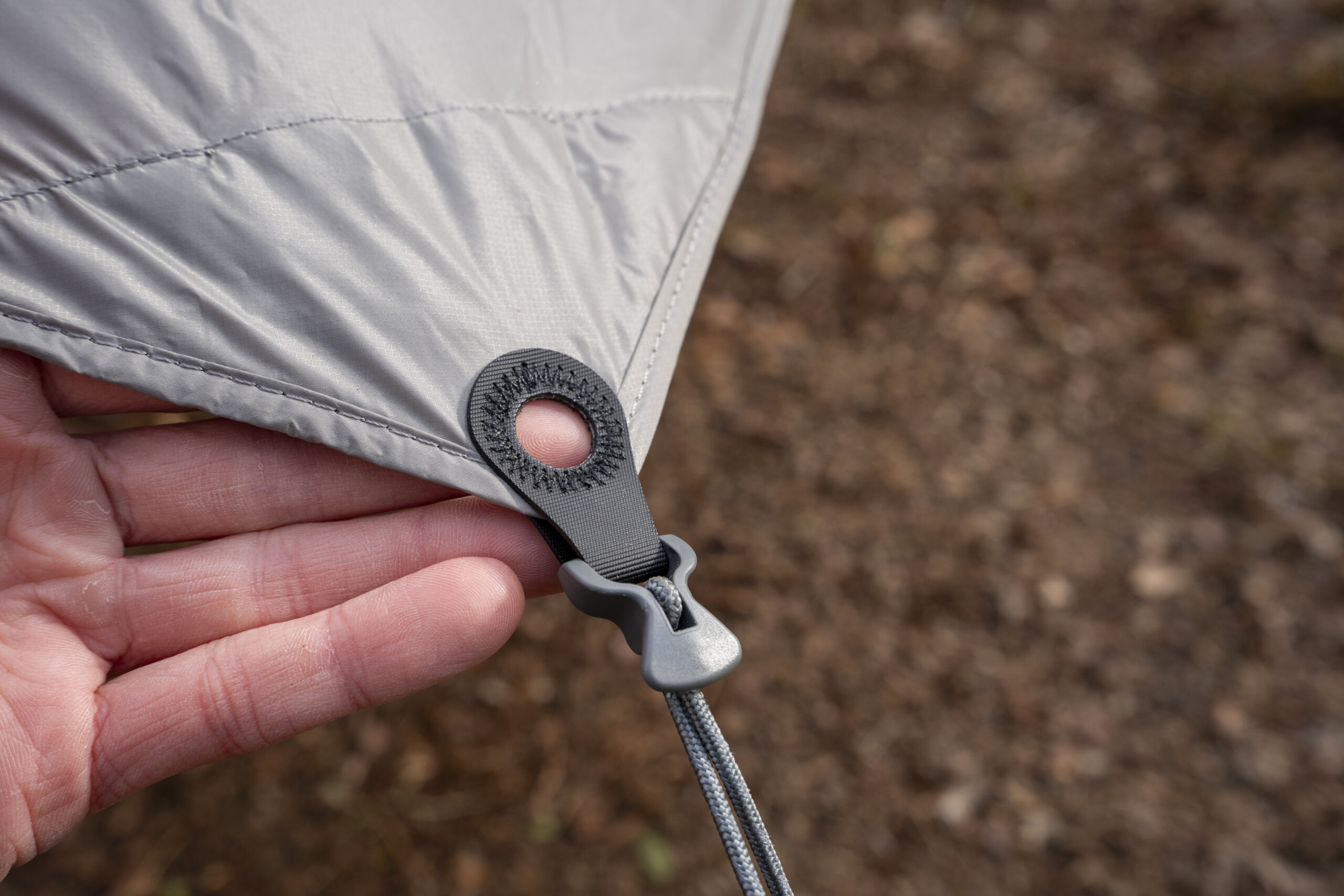 A hand points to a cord attached to a corner of a tarp