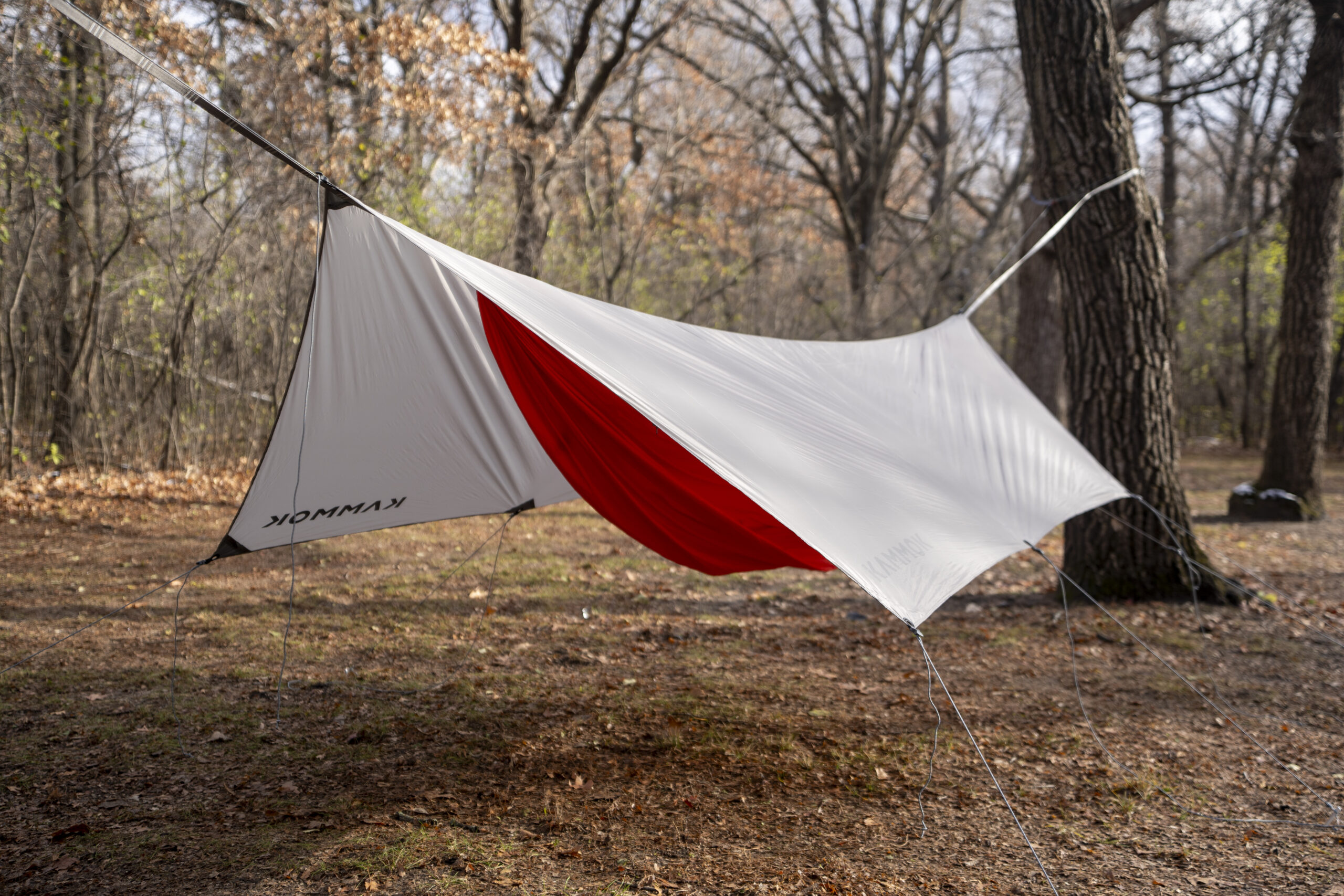 An orange hammock covered by a grey tarp in a forest