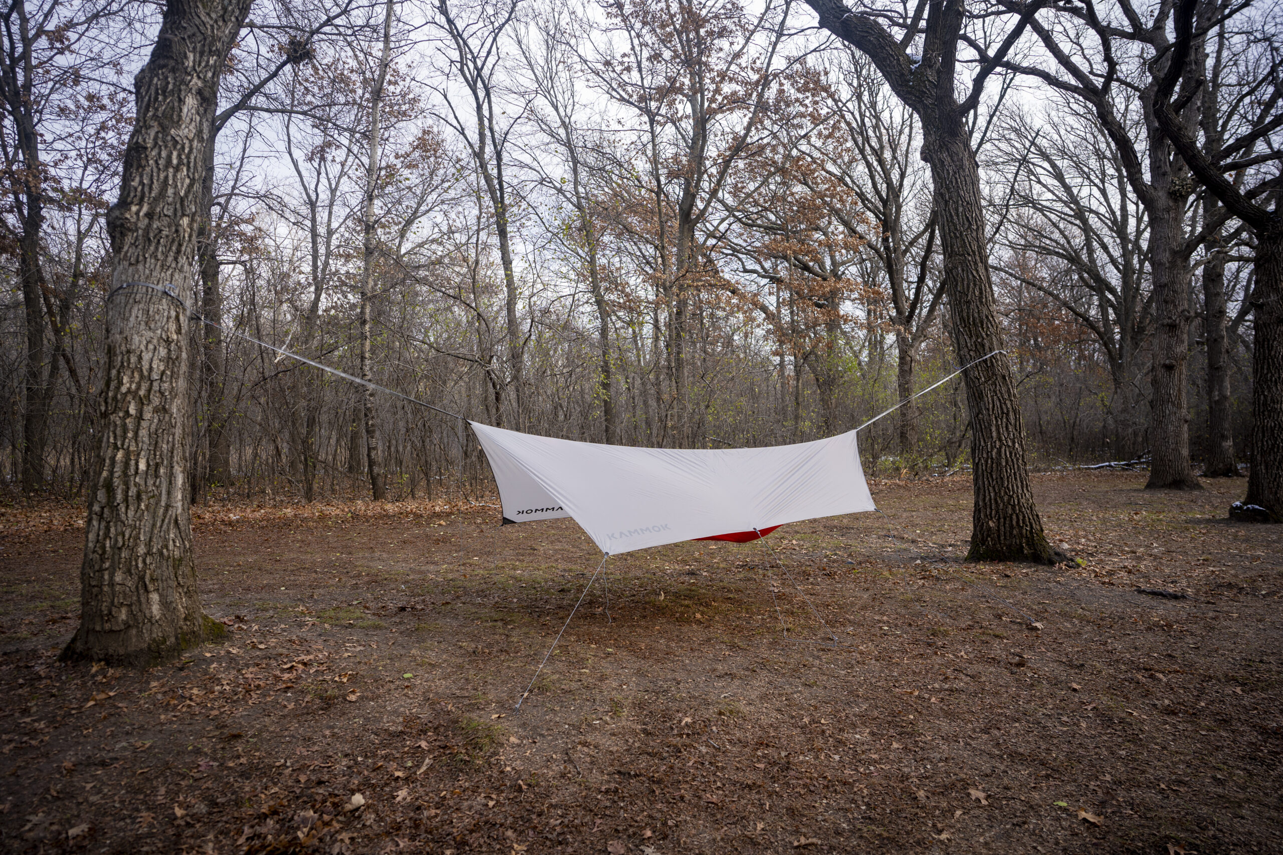 An orange hammock covered by a grey tarp in a forest clearing