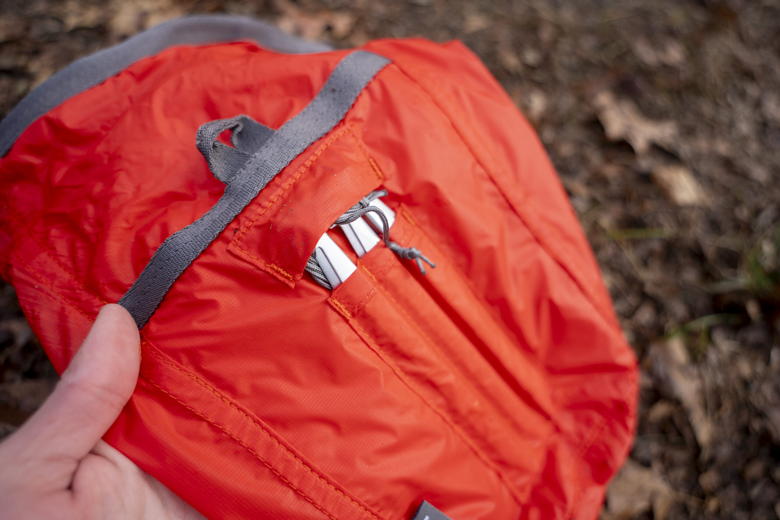 An orange bag with an exterior pocket for six tent stakes