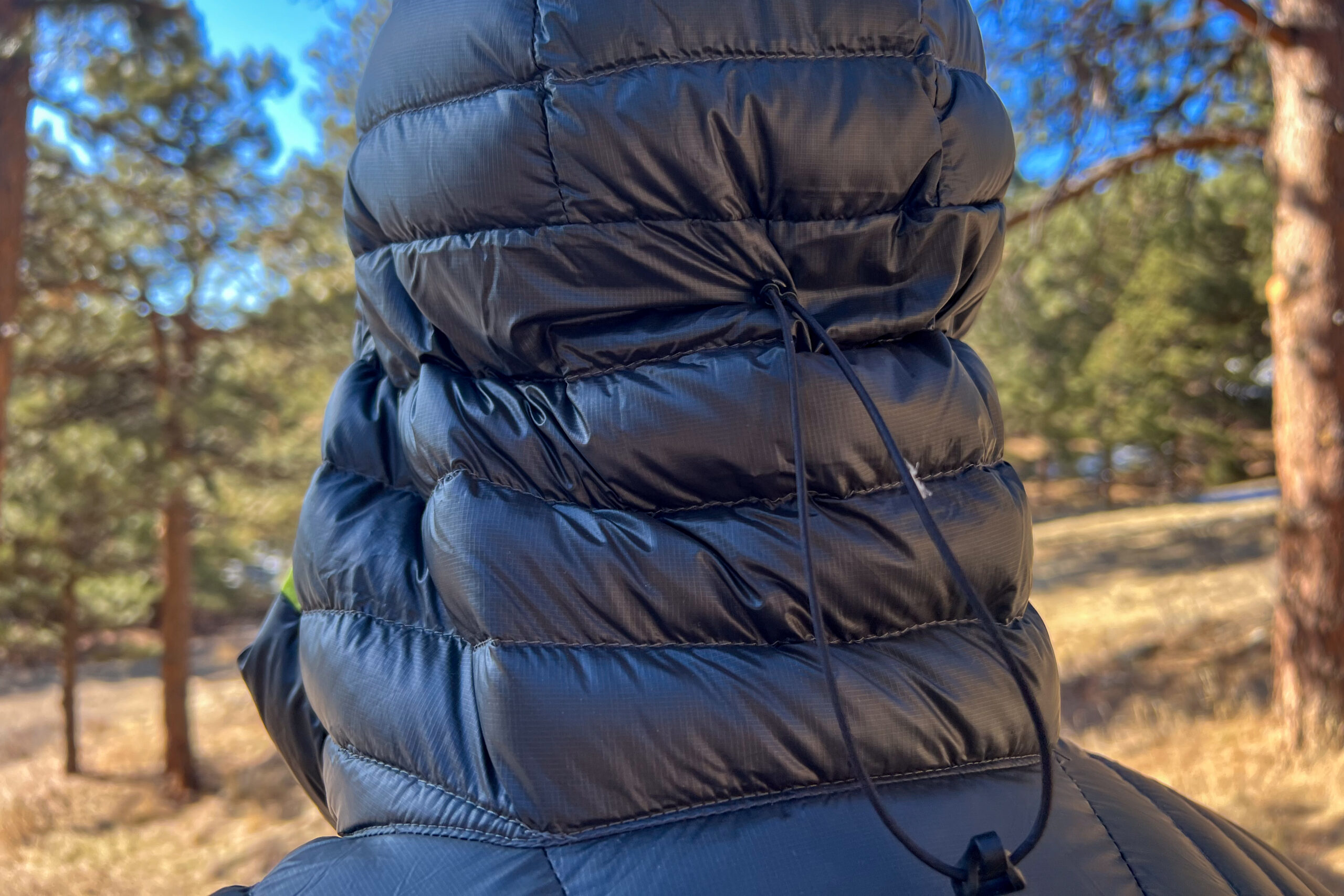 Back of a hooded down jacket showcasing horizontal baffles and a drawcord for fit adjustment.