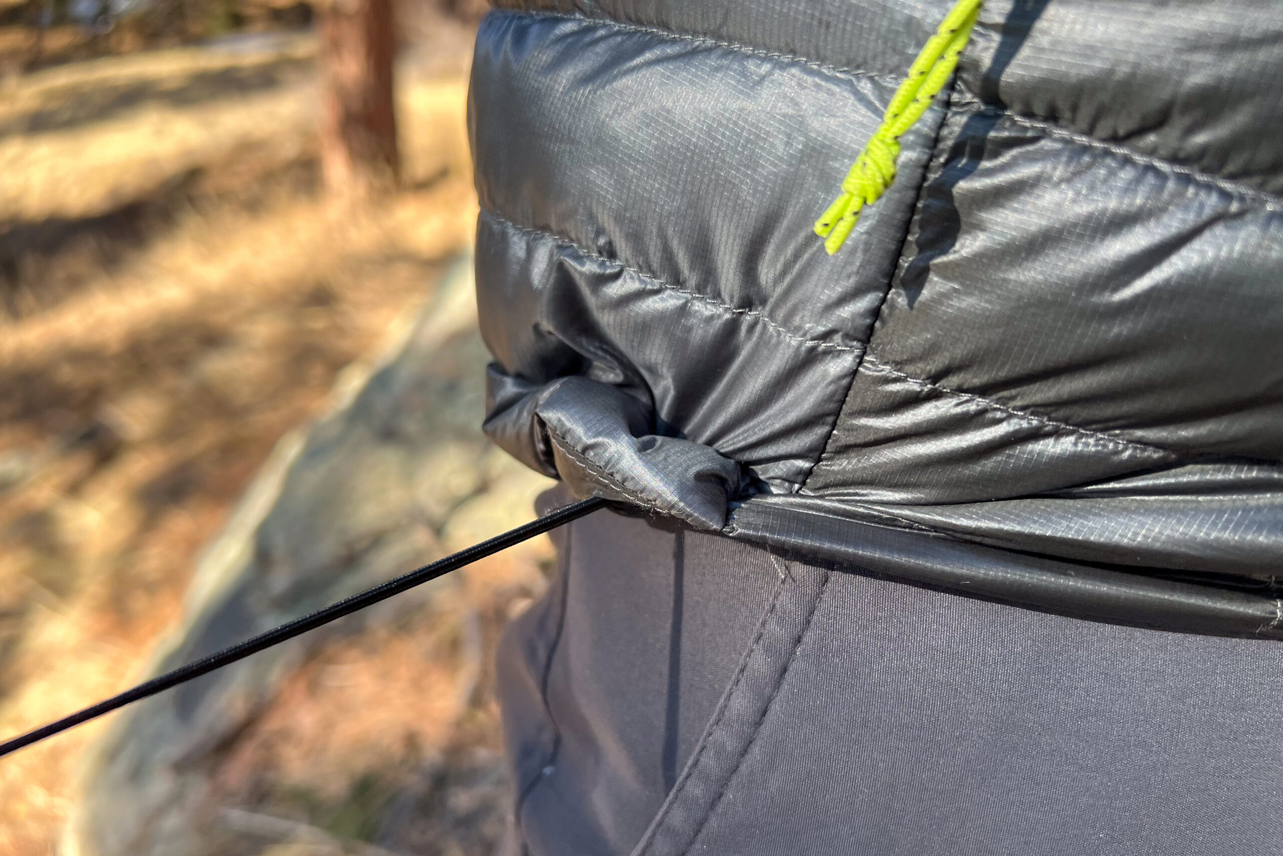 Close-up of the adjustable hem cinch cord on a down jacket being pulled tight for a secure fit.