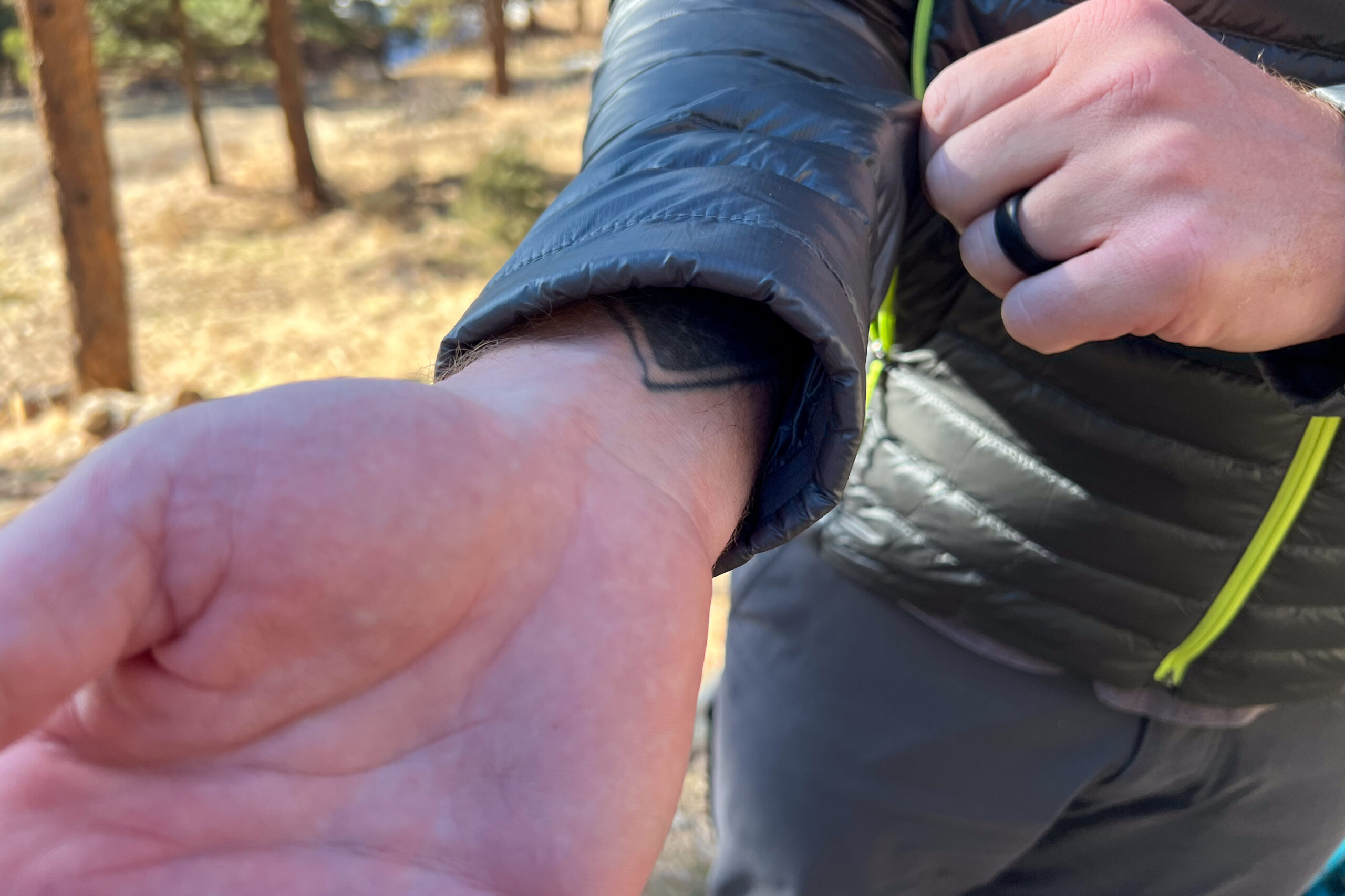 A close-up of a non-elastic cuff on a down jacket, loosely fitted around a person's wrist with a visible tattoo.