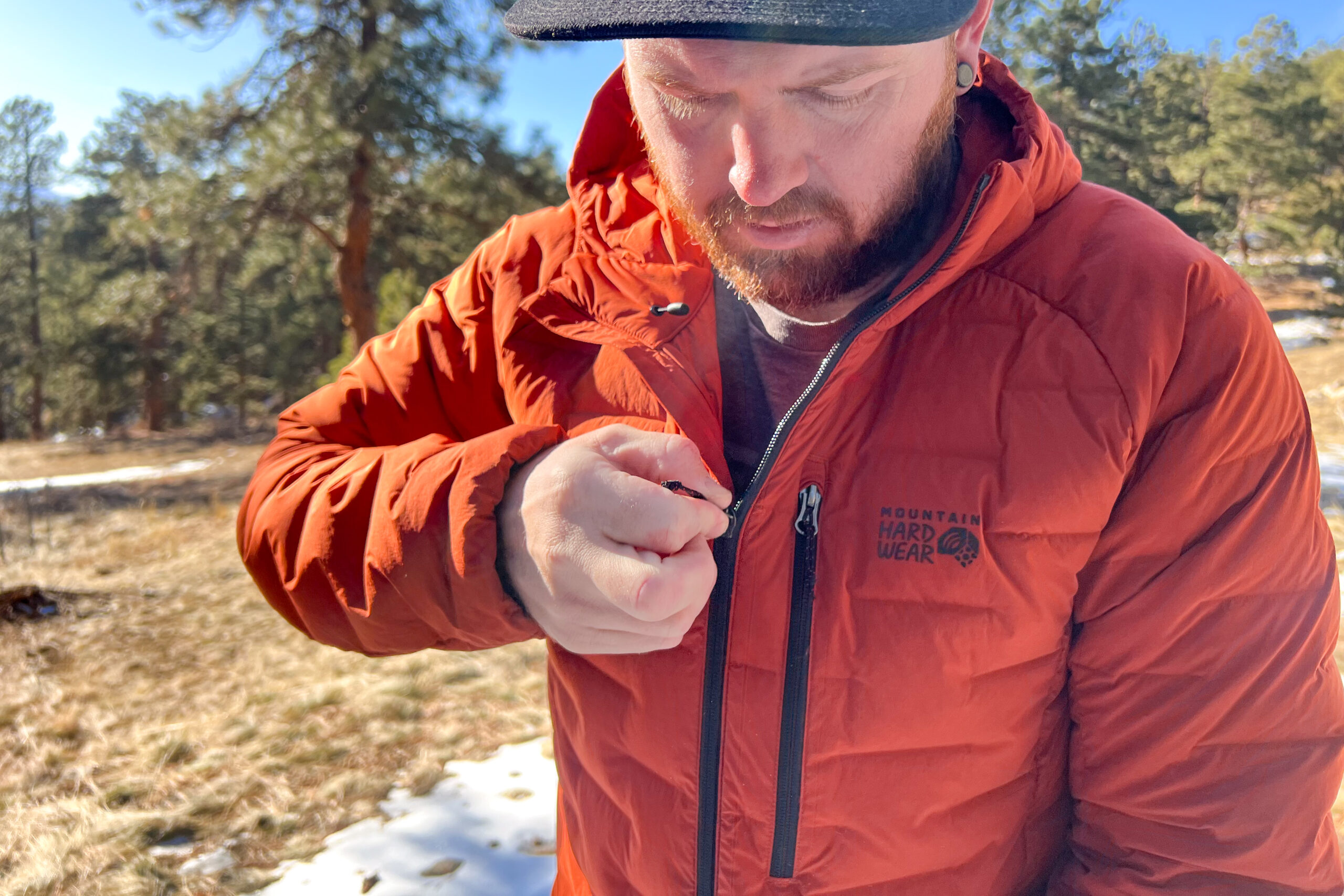 Close-up of a person zipping up the chest pocket on the Mountain Hardwear StretchDown Hoody, with the Mountain Hardwear logo visible.