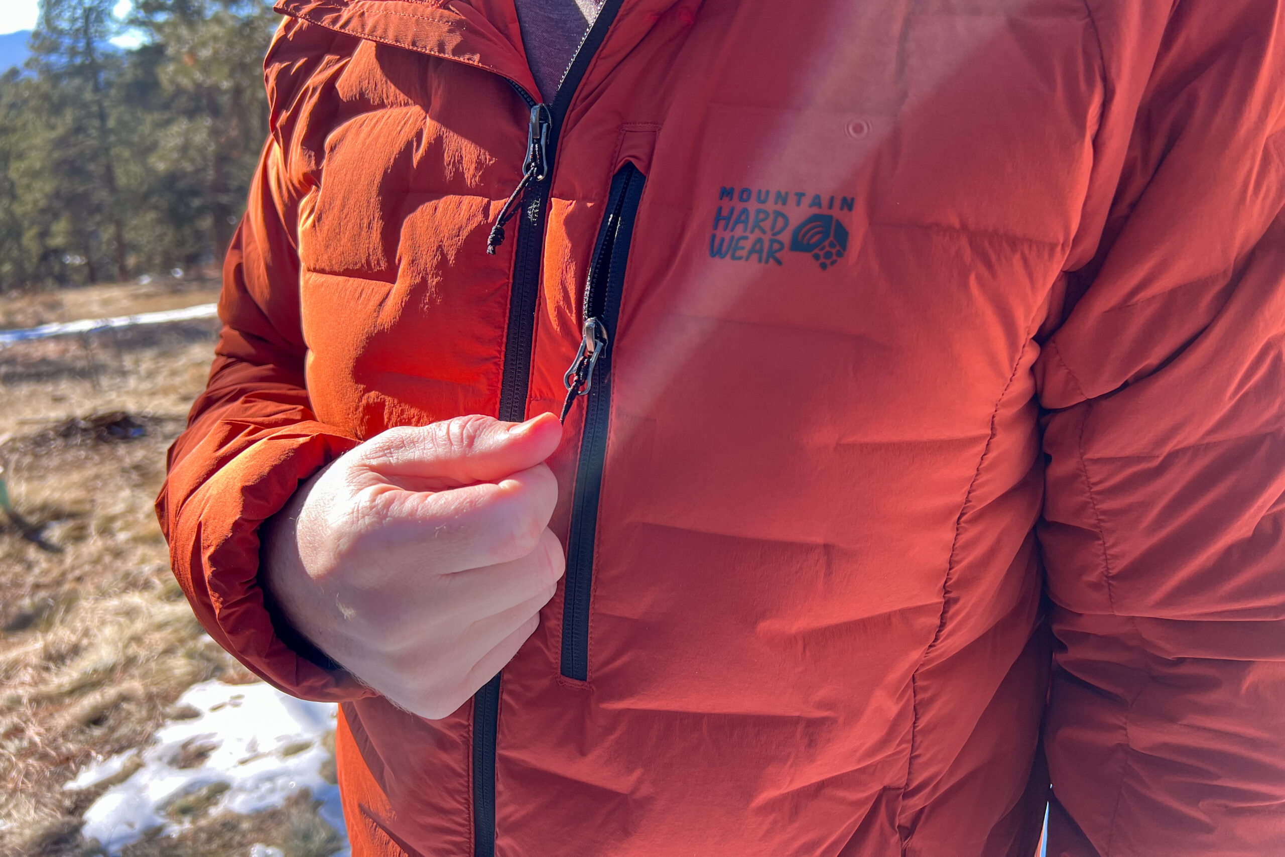 A close-up of a person pulling on the chest pocket zipper of the Mountain Hardwear StretchDown Hoody while outdoors.