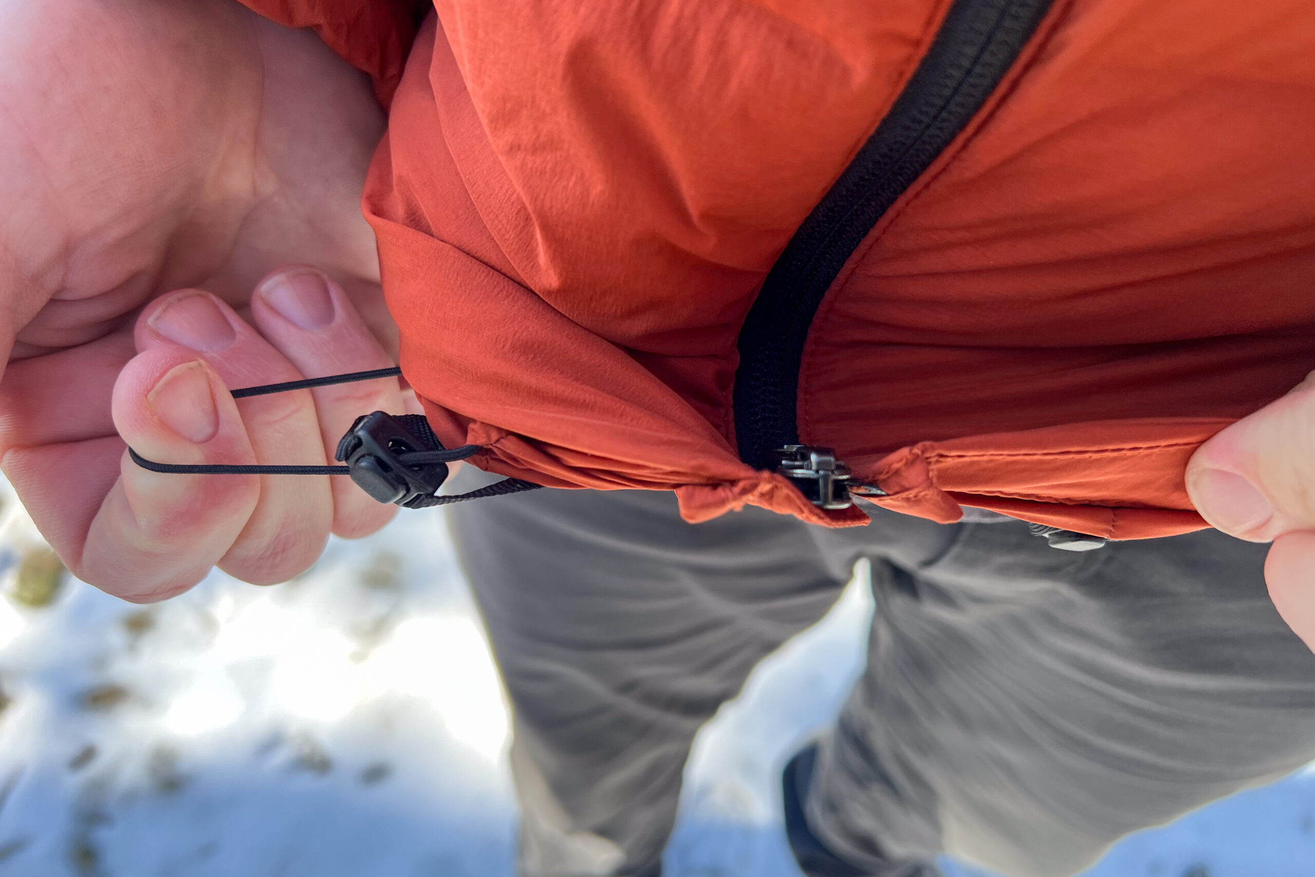 Close-up of a person adjusting the elastic hem cord of a Mountain Hardwear StretchDown Hoody, showing the drawstring toggle.