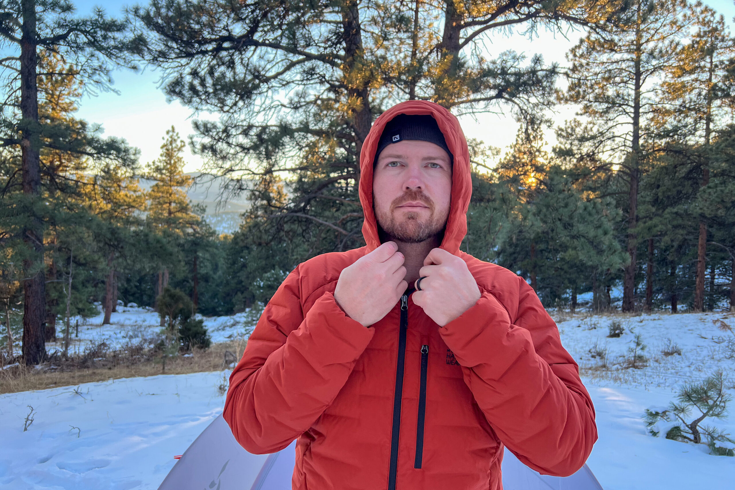 A person adjusting the hood of the Mountain Hardwear StretchDown Hoody in a snowy forest with trees in the background.