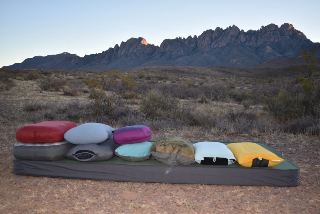 Camp pillows stacked on a sleeping pad from thickest (left) to thinnest (right) with rugged mountains in the background