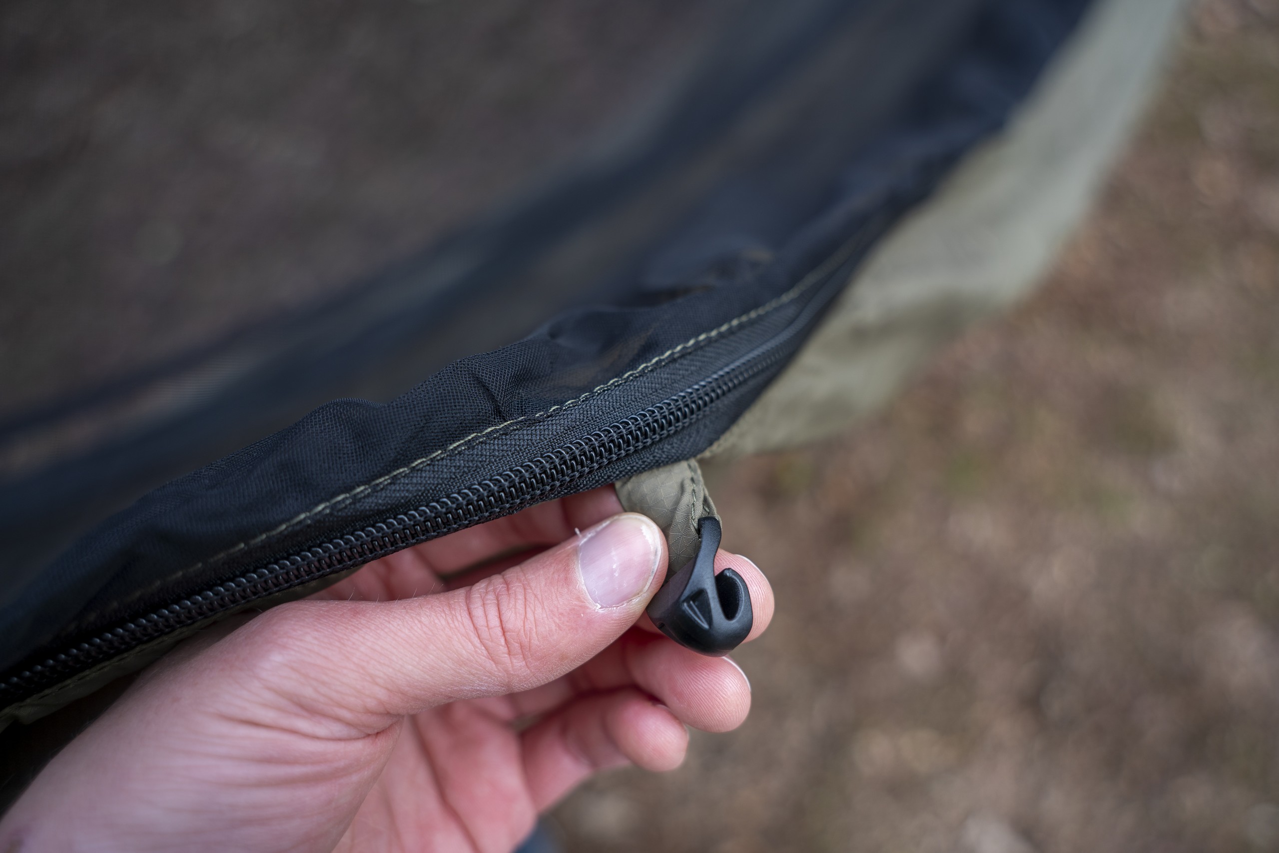 a hand holds an underquilt hook on a hammock