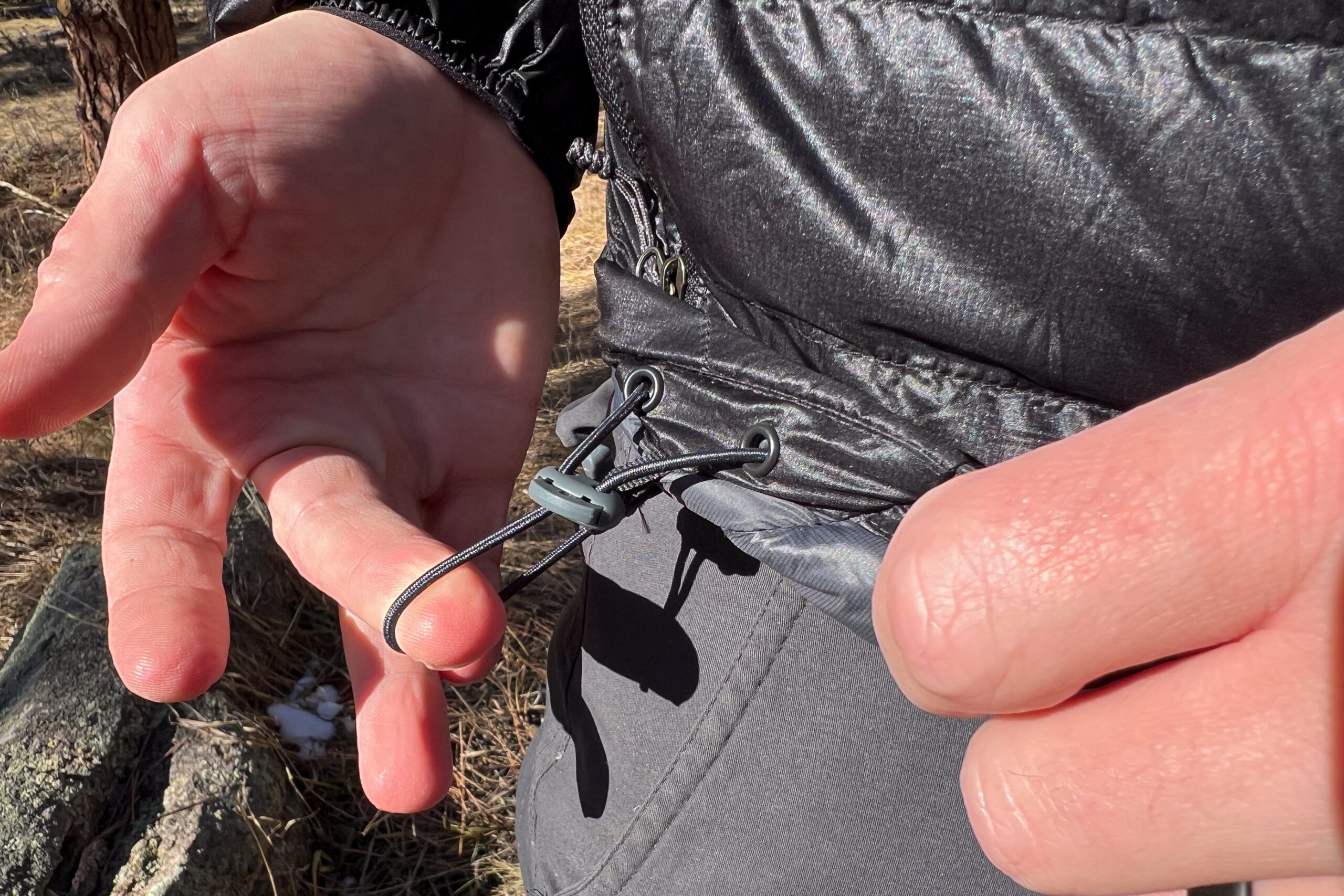 Close-up of a hand adjusting the drawcord hem on the Outdoor Research Helium Down Hoody, showing the elastic cinch system.