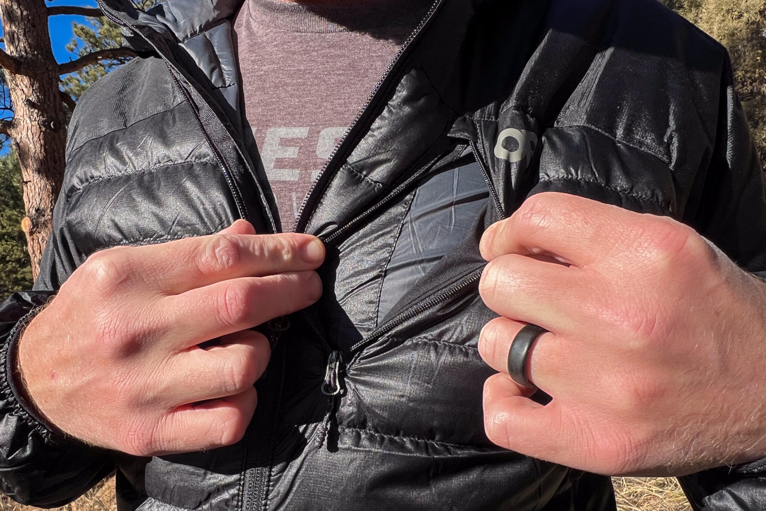 Close-up of a person unzipping the chest pocket of the Outdoor Research Helium Down Hoody to reveal a phone inside.