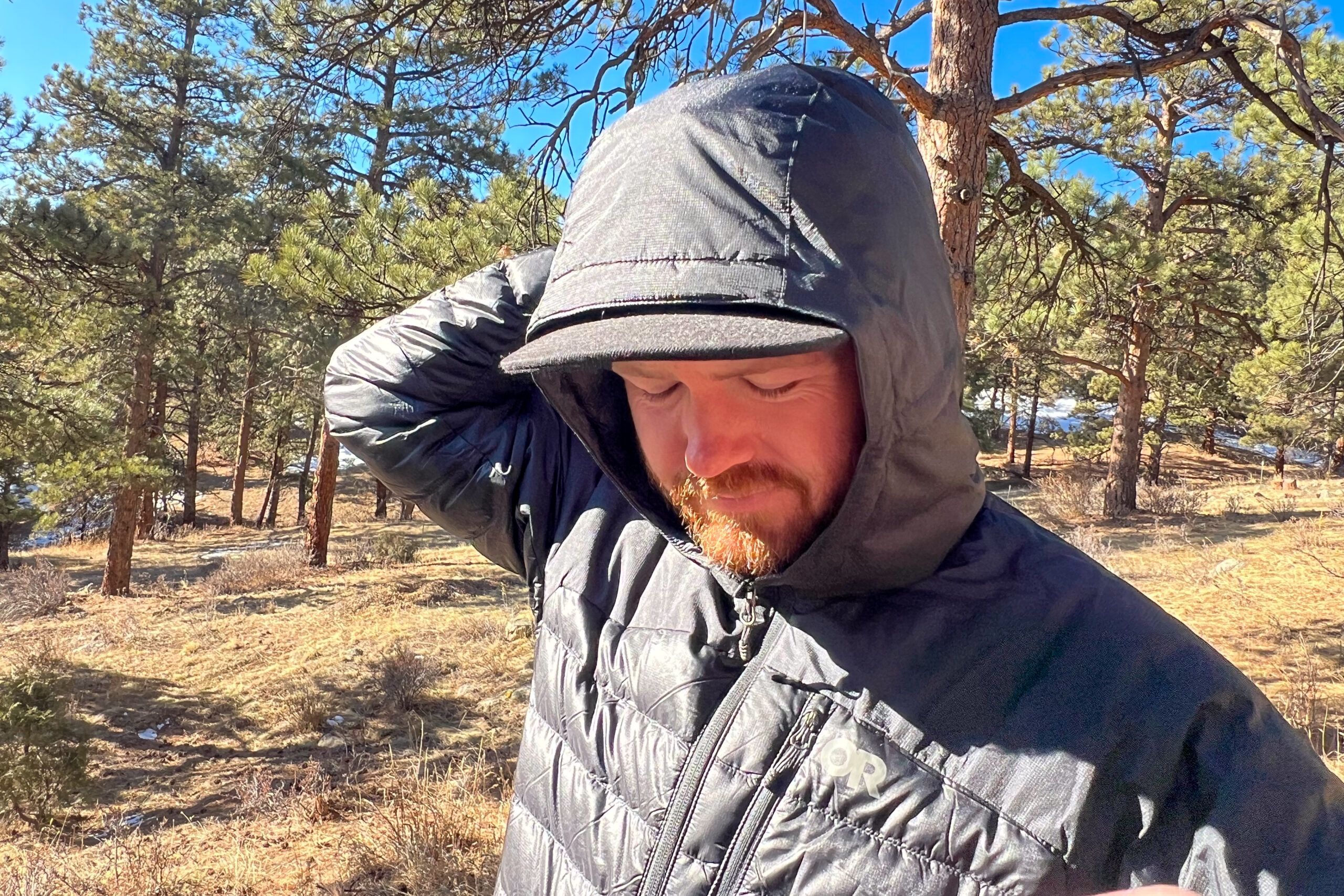 Person wearing the Outdoor Research Helium Down Hoody with the hood up, showing its waterproof and durable fabric.