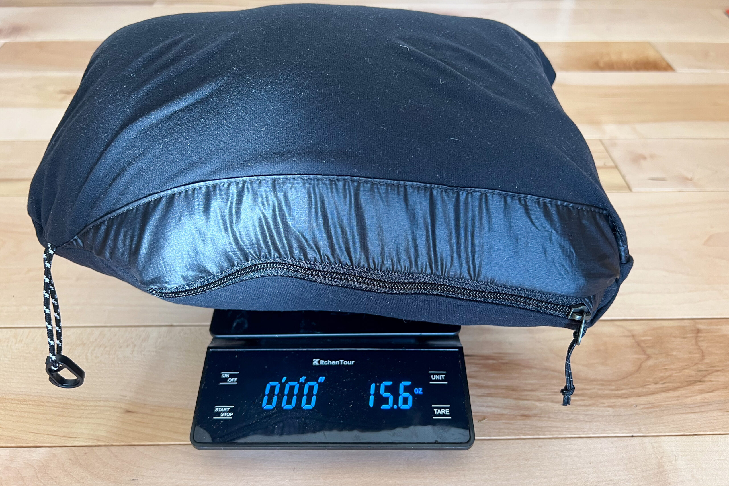 The Outdoor Research Helium Down Hoody packed into its pocket on a scale, displaying a weight of 15.6 ounces.