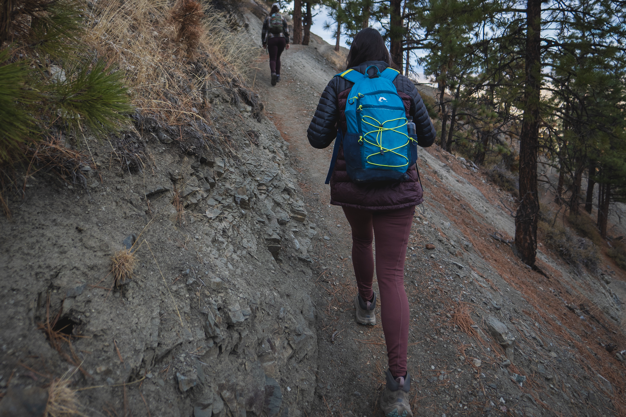 woman hiking uphill in pastel pink leggings and blue backpack