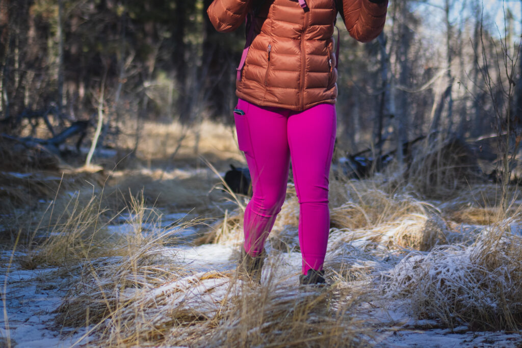 Person hiking in bright pink leggings, wearing a bronze down jacket and black gloves.