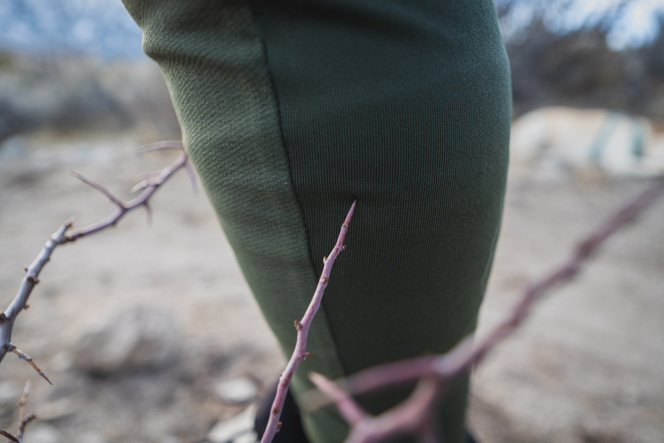 Woman hiking on dirt trail in high desert terrain, wearing forest green hiking leggings with pockets, around sunset.