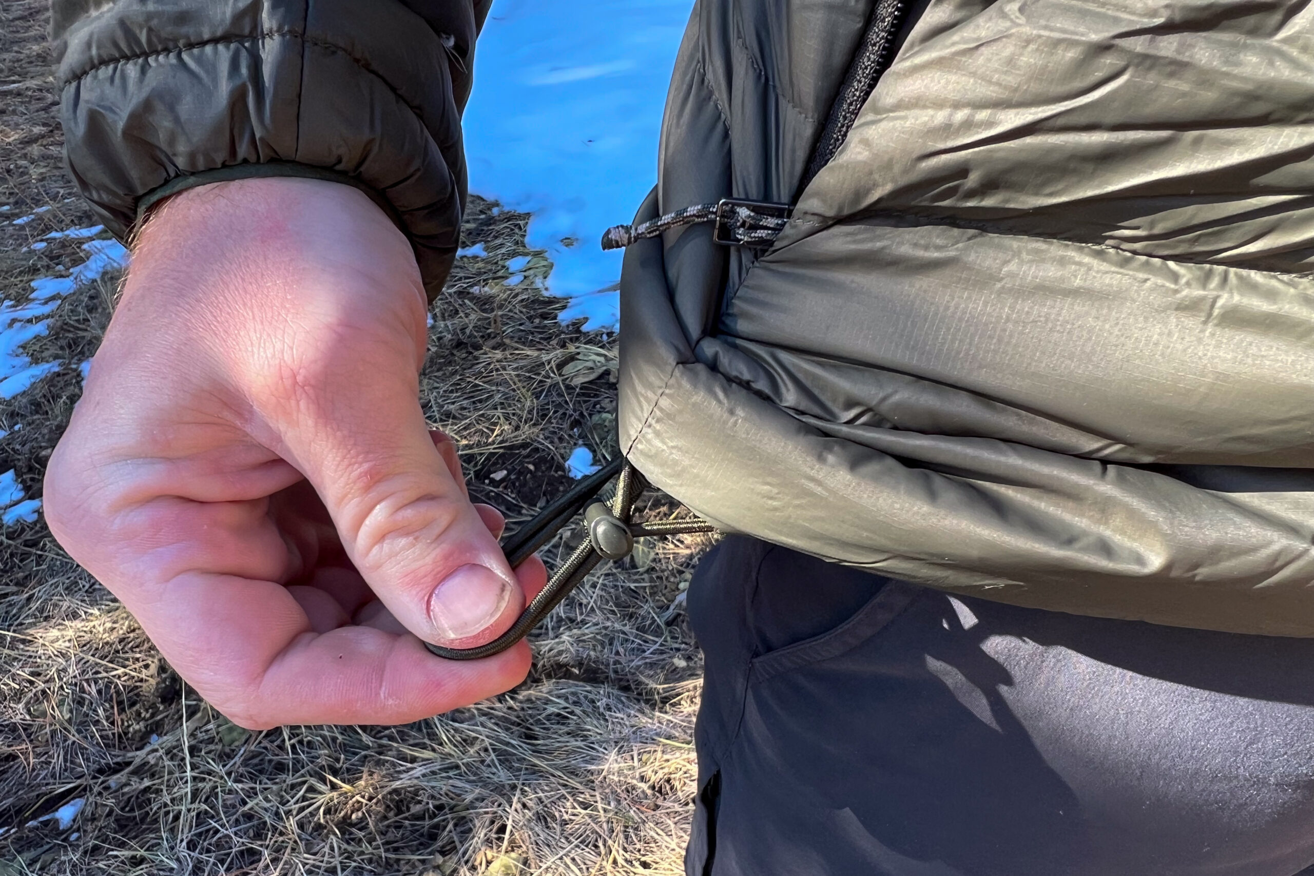 A person tightening the drawcord hem on the Patagonia Down Sweater Hoody, showing its adjustable bottom for a snug fit.