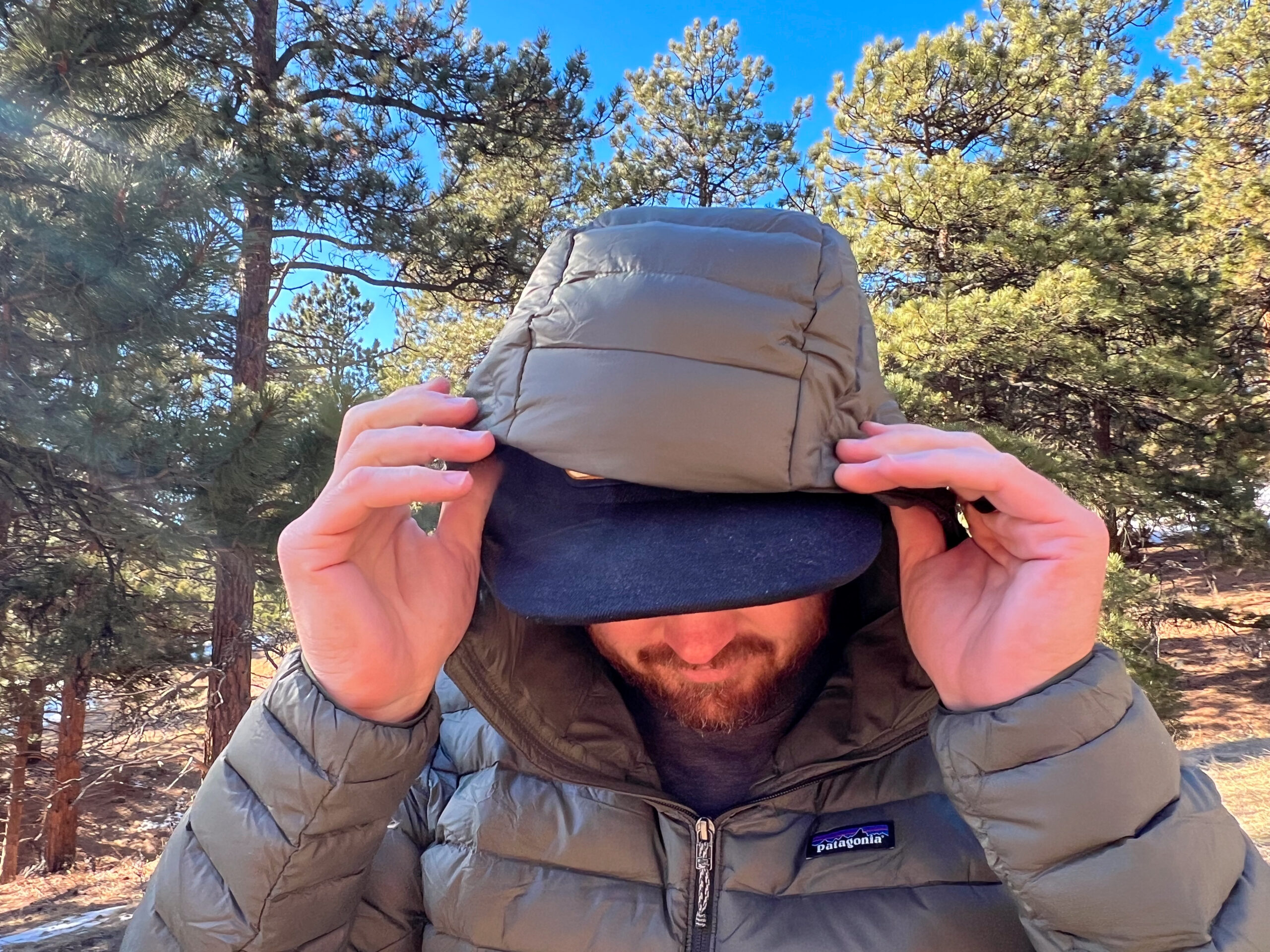 A person adjusting the hood of the Patagonia Down Sweater Hoody while wearing a baseball cap, highlighting the hood's size and coverage.