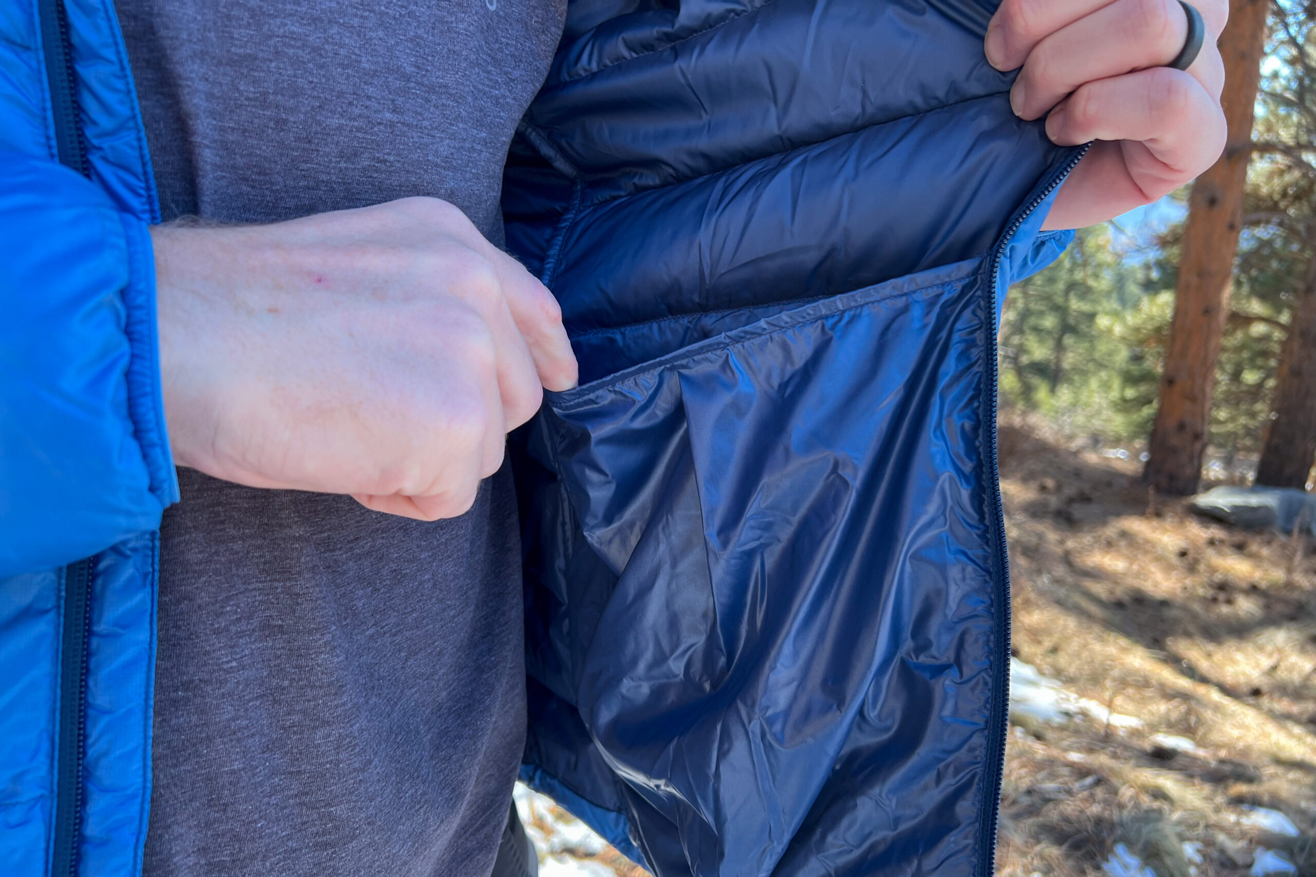 A close-up of the REI 650 Down Jacket’s interior drop pocket with a hand demonstrating its depth and storage capacity.