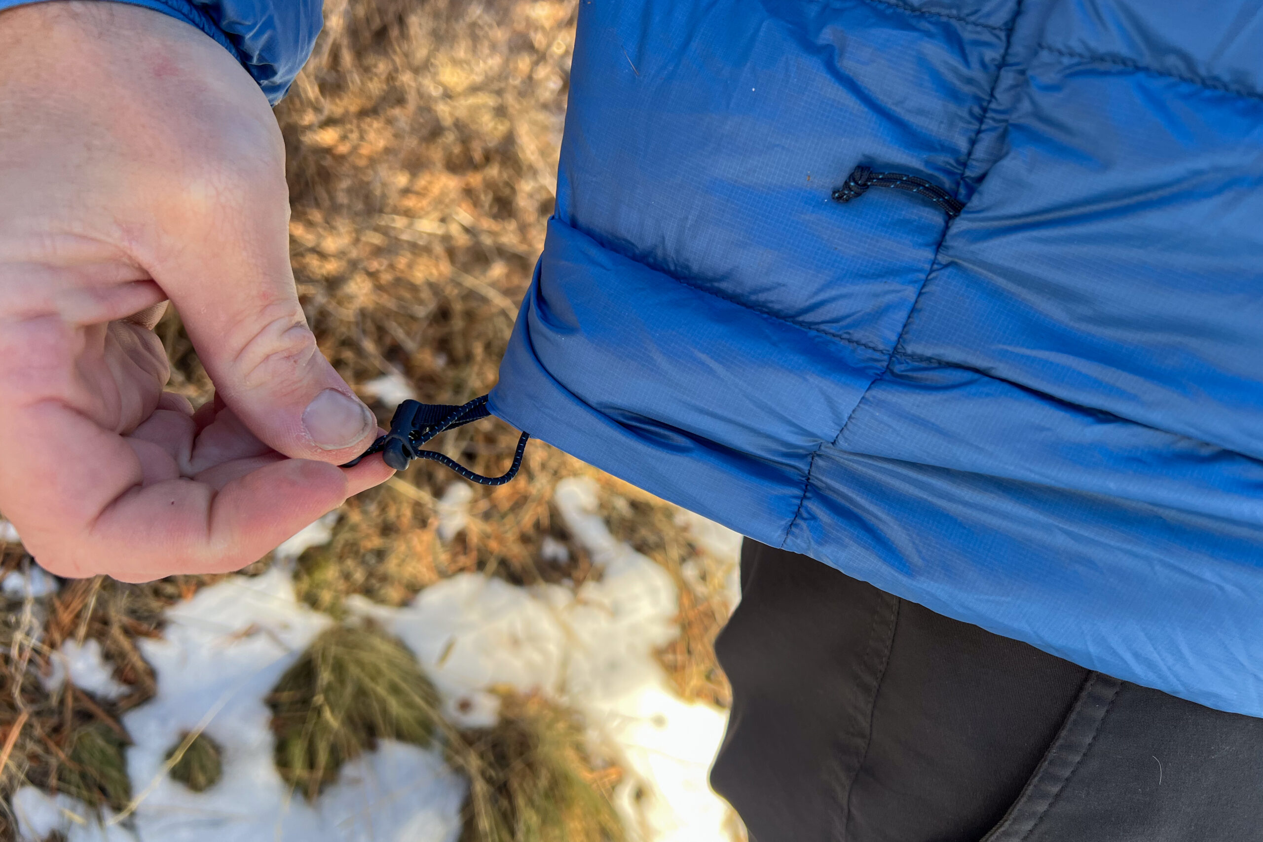 A hand pulling the adjustable hem cord on the REI 650 Down Jacket, showcasing the cinch feature for draft control.