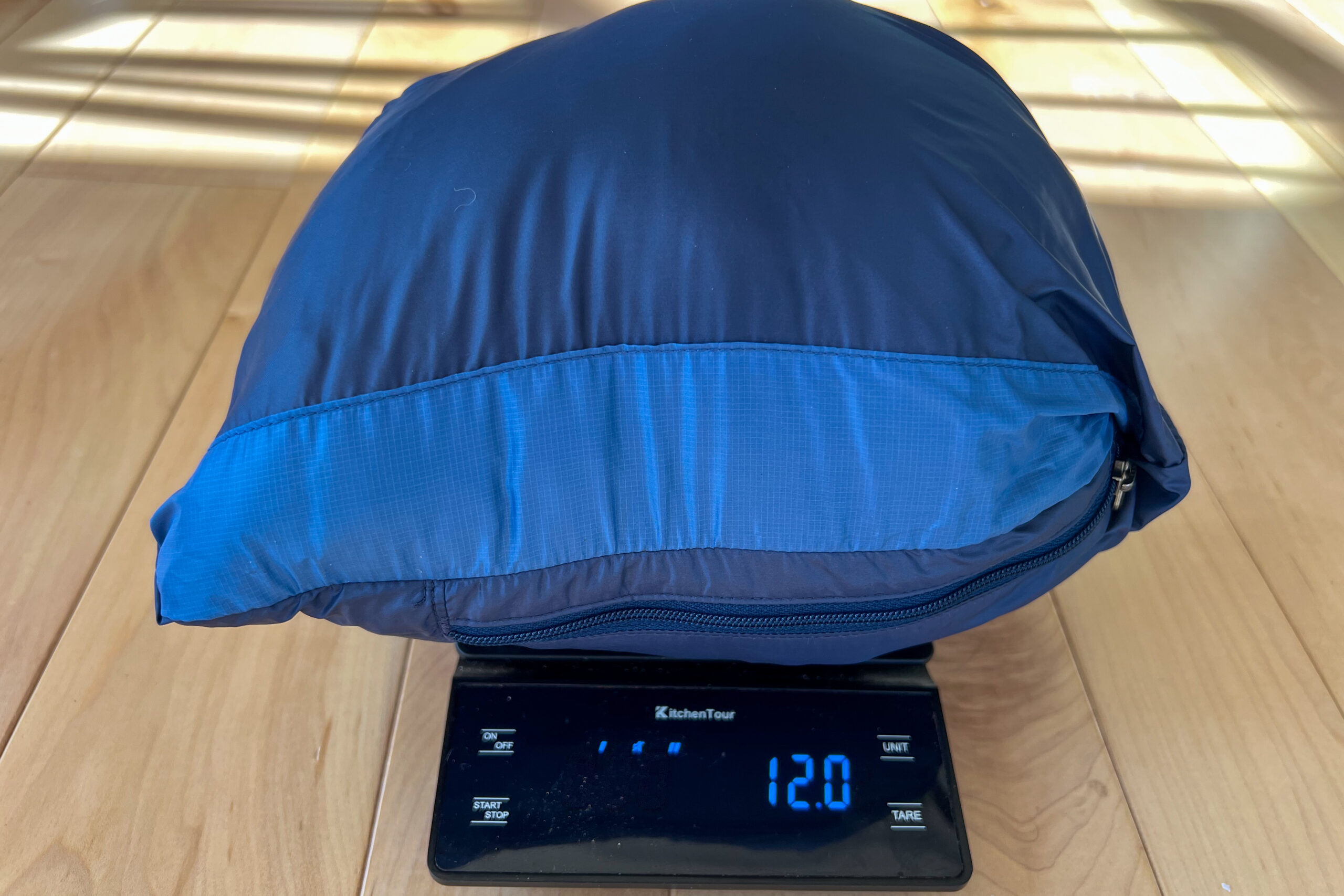 The REI 650 Down Jacket packed into its pocket, sitting on a scale that displays a weight of 12.0 ounces.