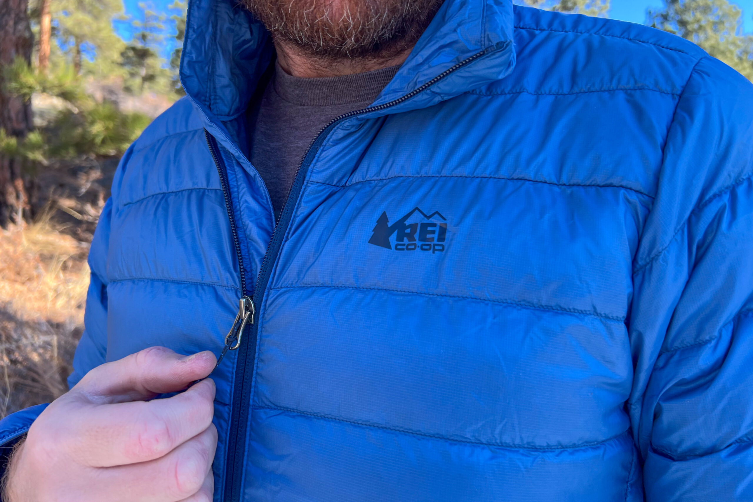 Close-up of a person zipping up the REI 650 Down Jacket, showcasing the REI Co-op logo on the left chest and smooth front zipper.