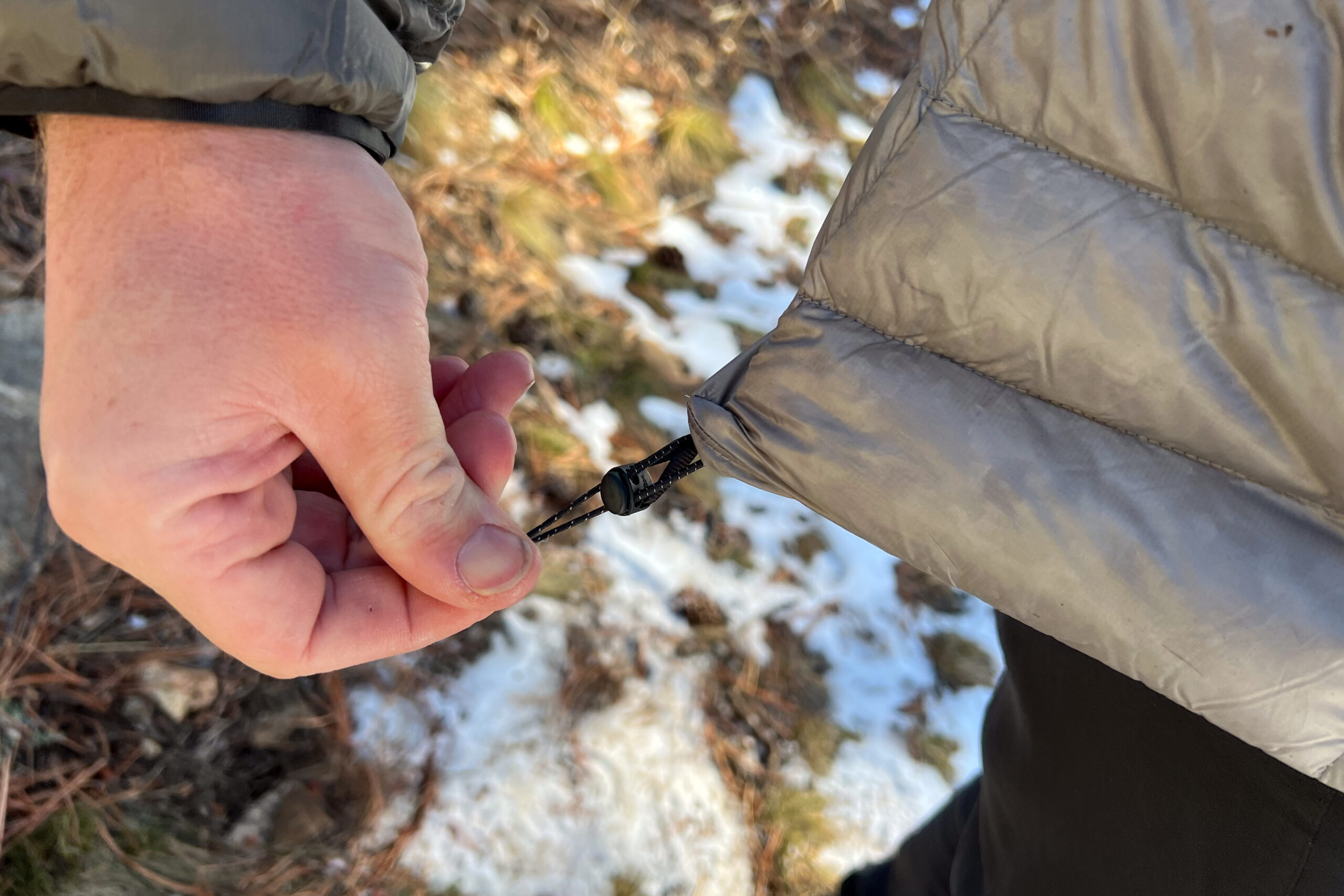 Close-up of a person tightening the drawcord hem of the REI Magma 850 Down Hoody.