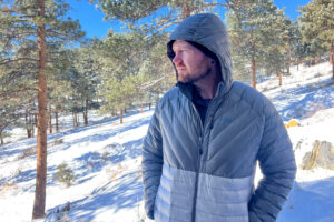 Person standing in a snowy forest wearing the REI Magma 850 Down Hoody, facing sideways with the hood up.