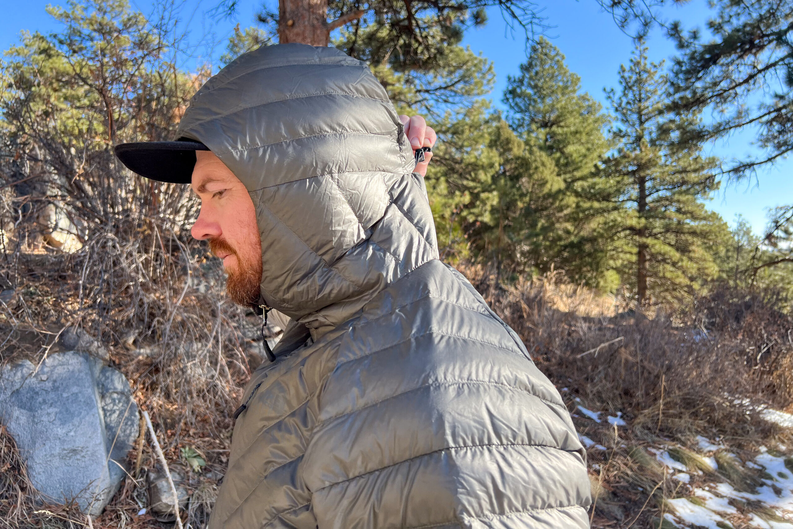 Person wearing the REI Magma 850 Down Hoody with the hood pulled up, showing its side profile in a forested setting.