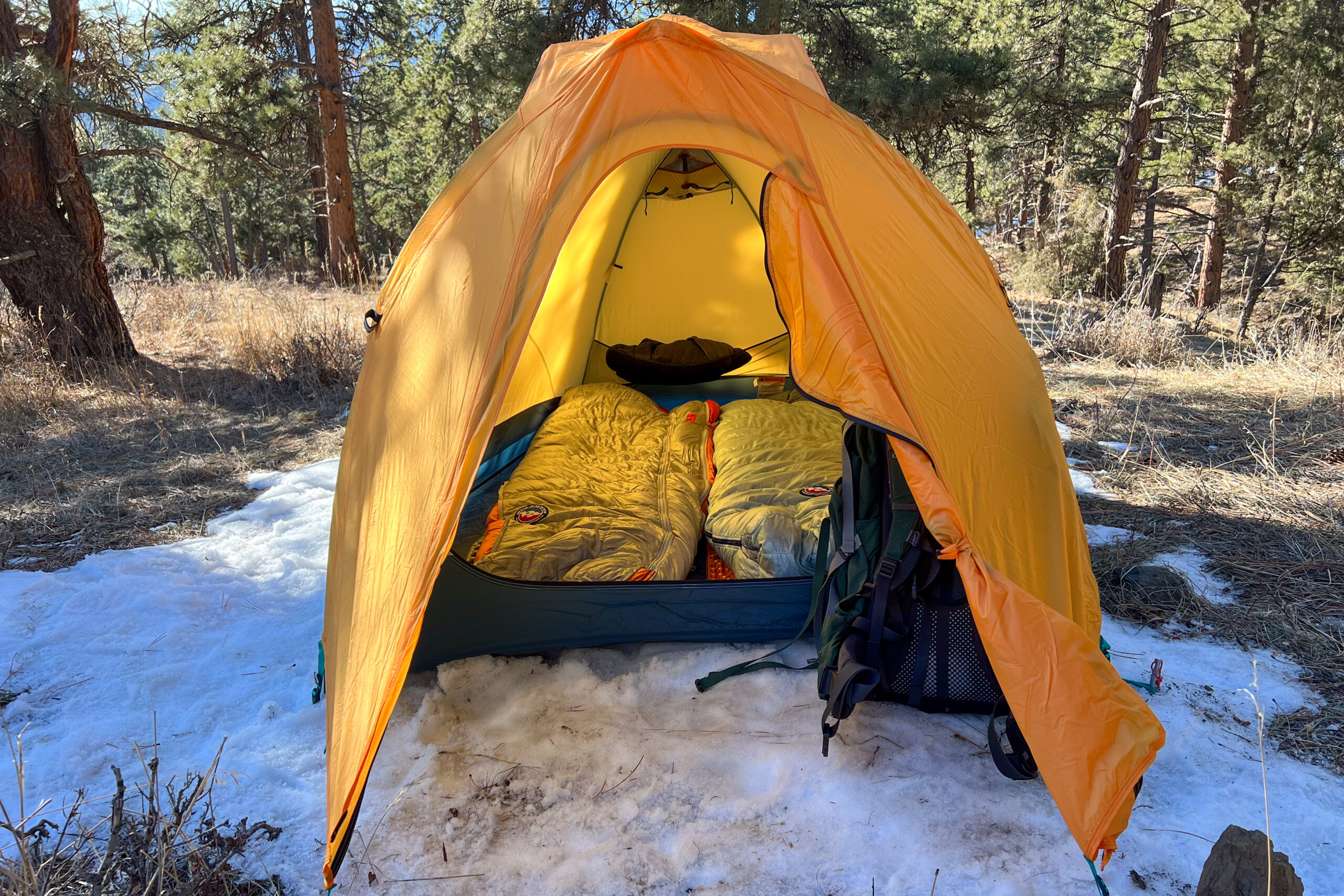 An orange tent facing the camera. Both the vestibule door and tent door are open showing sleeping bags inside.