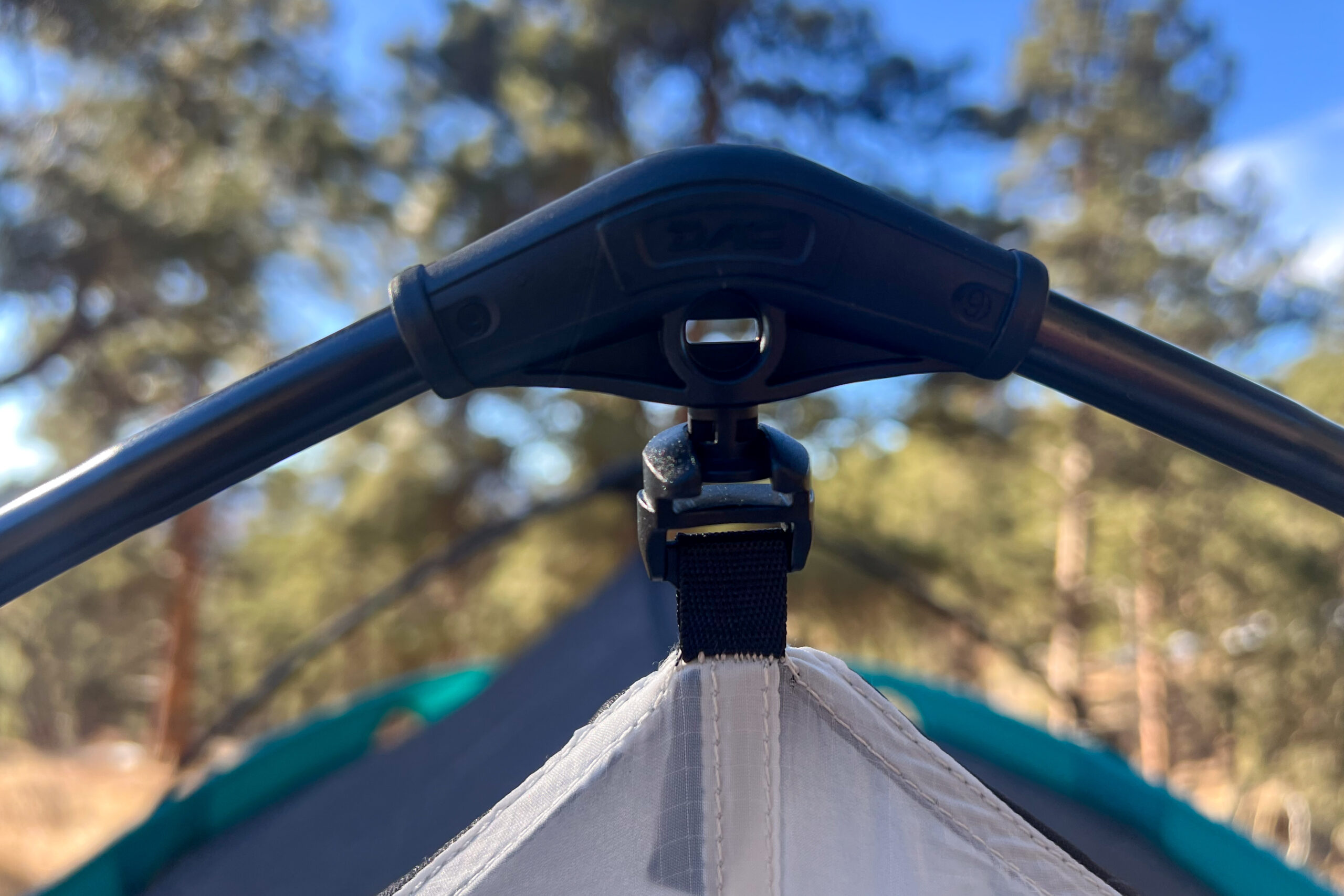 A close up shot of an attachment point of a tent. There a blurry trees in the background.