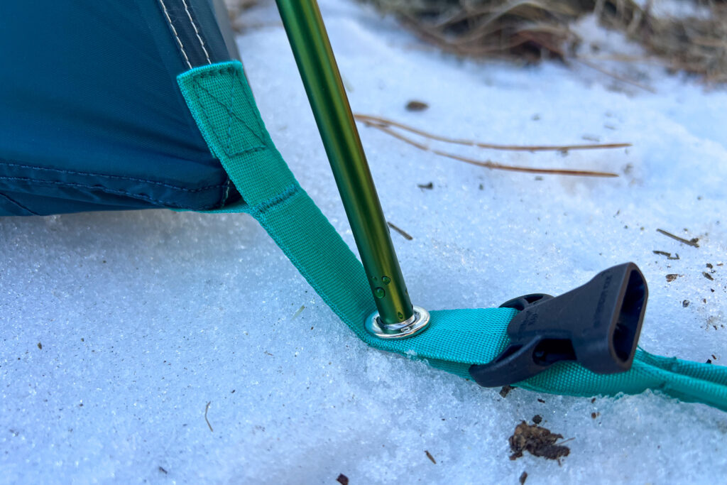 A close up shot of the corner webbing and grommet of a tent laying on the snow.