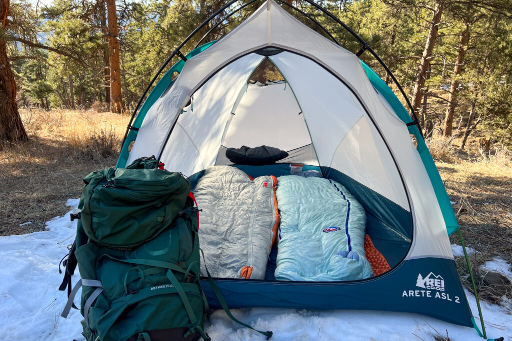 A tent, pithed on a small patch of snow in a forested setting. The fly is not on the tent and the door is wide open.