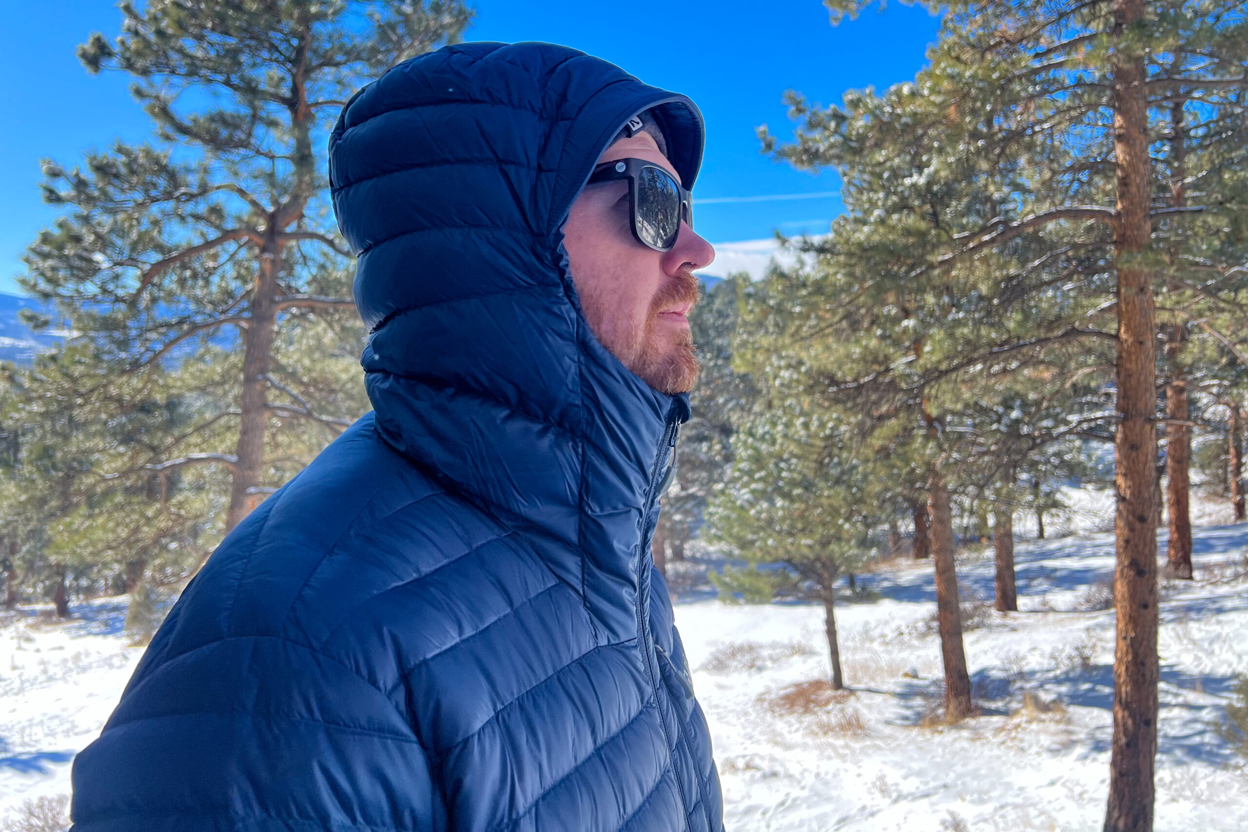 A side profile of a person in the Rab Microlight Alpine jacket, with the hood up, showcasing its full coverage and insulated protection.