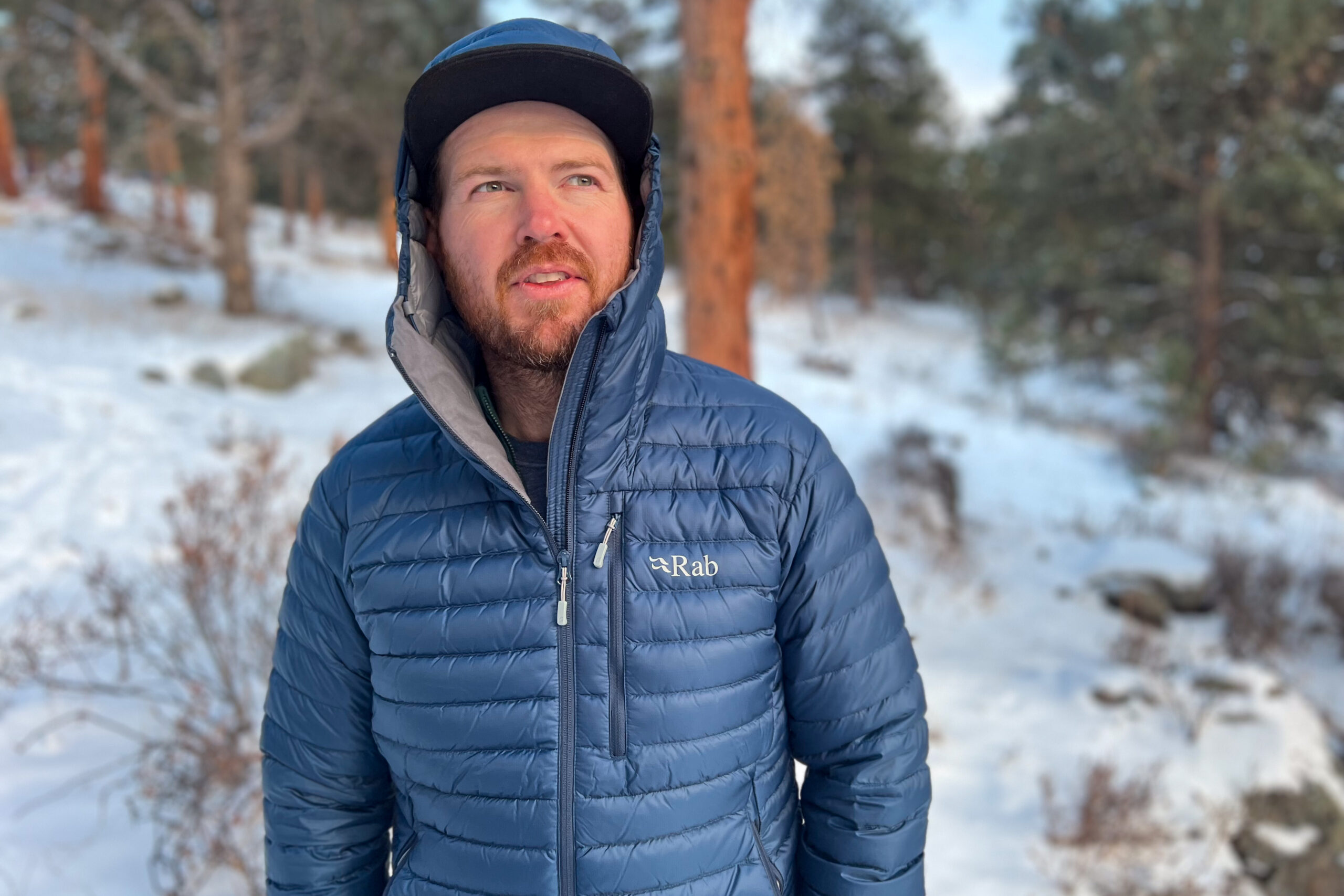 A person wearing the Rab Microlight Alpine jacket with the hood up and partially unzipped, showcasing its fit and interior lining.