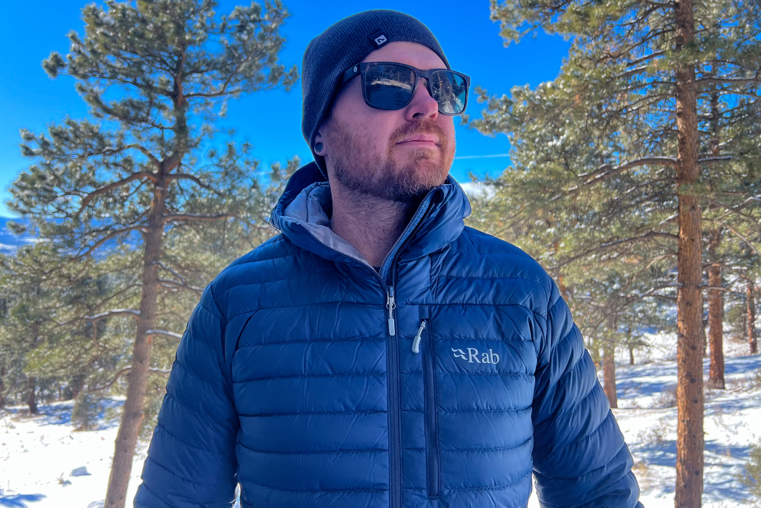 A person wearing the Rab Microlight Alpine jacket in a snowy forest, showing its insulated design and sleek fit for cold conditions.